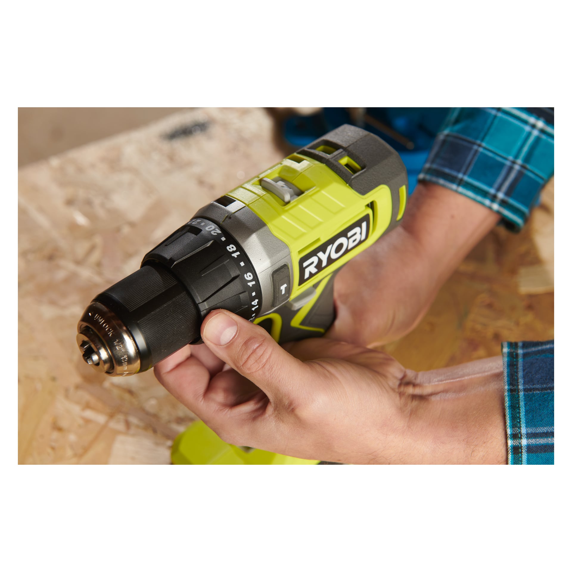 En person i blå rutiga ärmar justerar inställningarna på en grön Ryobi One+ Impact borrmaskin RPD18-0, med en träarbetsyta under.