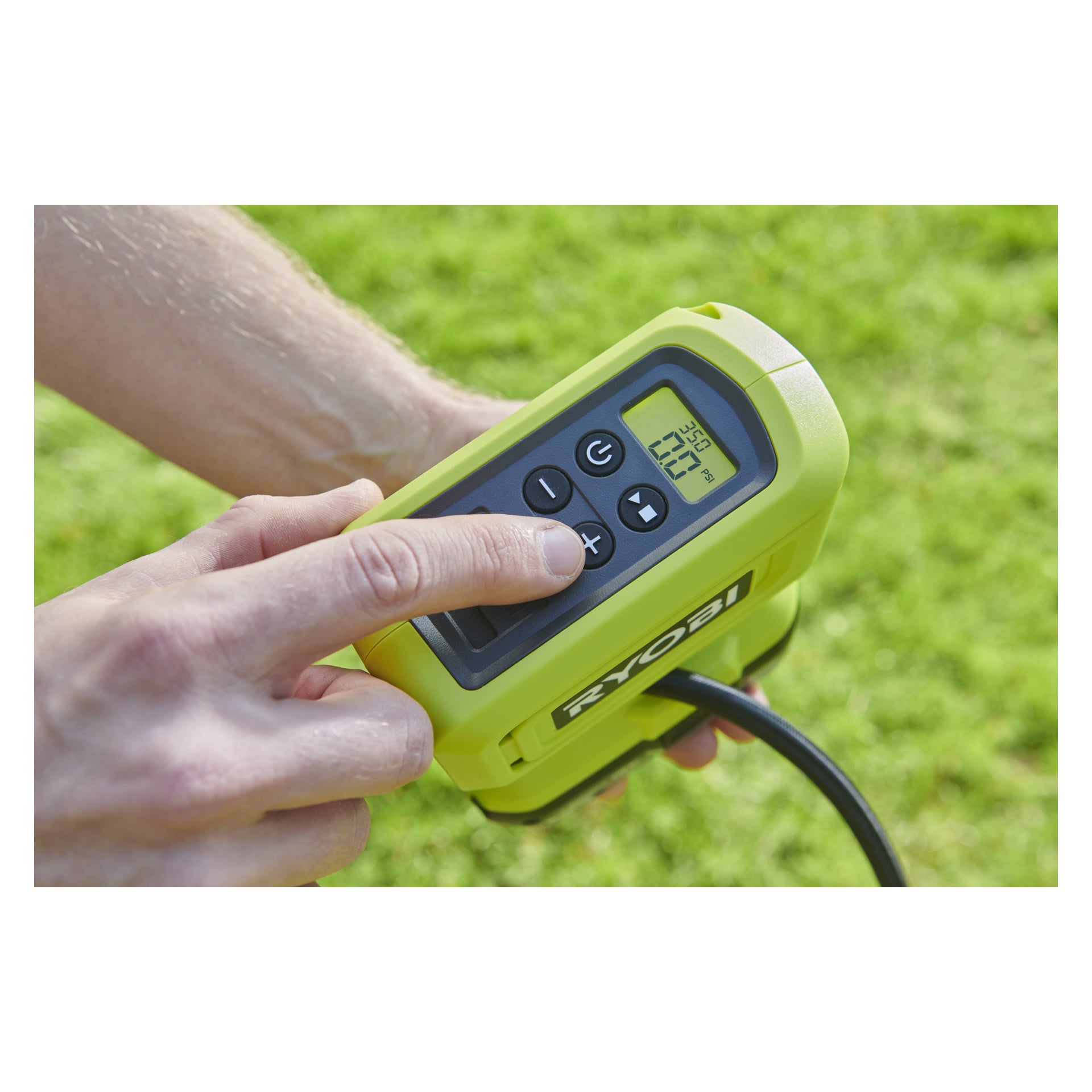Ręka obsługuje przycisk w Ryobi One+ zasilanym bateriami mini pompą powietrza RPI18-0 z widoczną na cyfrowym wyświetlaczu "35,0 PSI". Zielone urządzenie, które ma wiele przycisków, jest używane na trawie na zewnątrz.