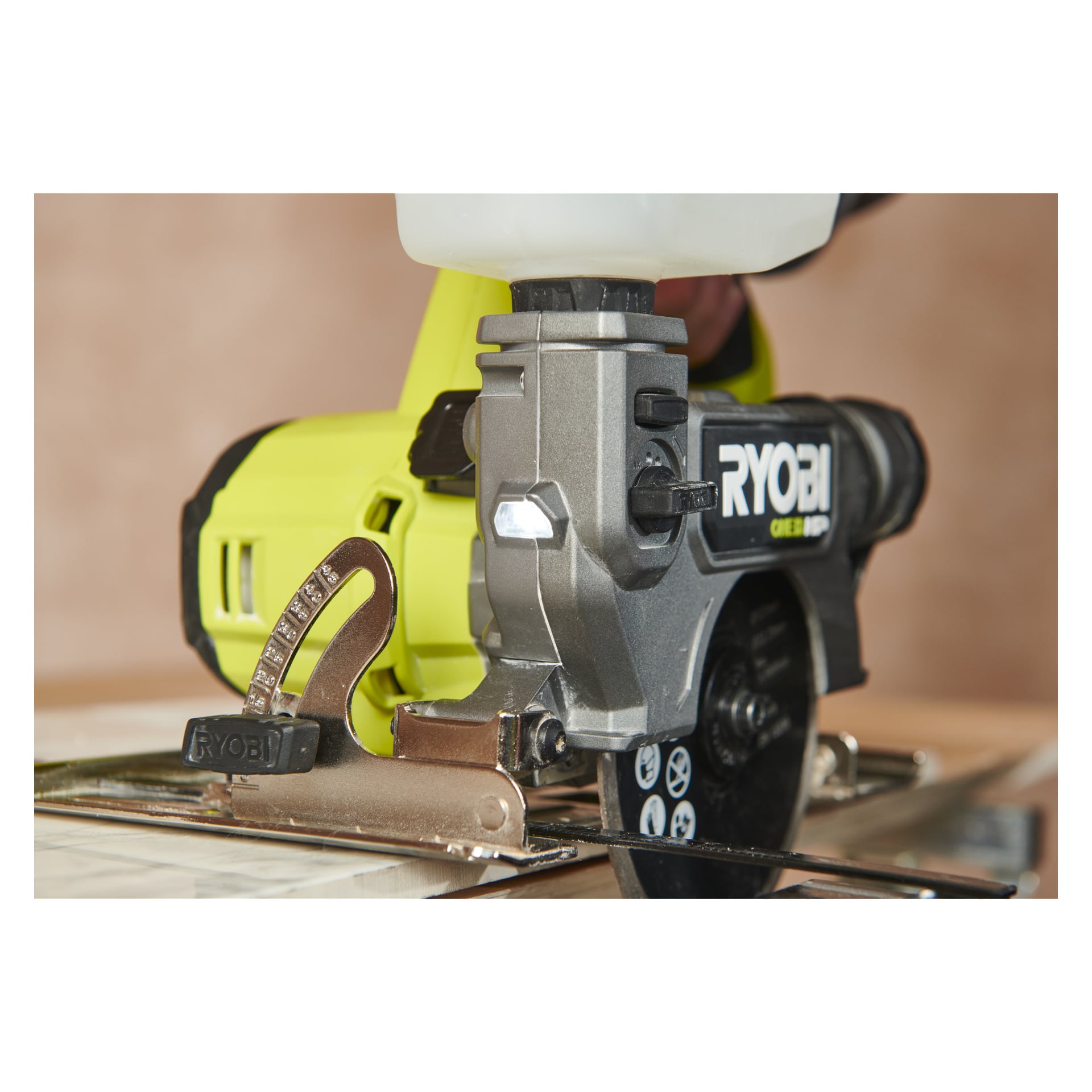 Detaljerad vy av en Ryobi One+ HP sladdlös platta och klinker såg RTS18C-0 i drift, där den skar genom en ruta. Verktyget körs med en ansluten vattenreservoar och Ryobi-logotypen finns på dess sida.