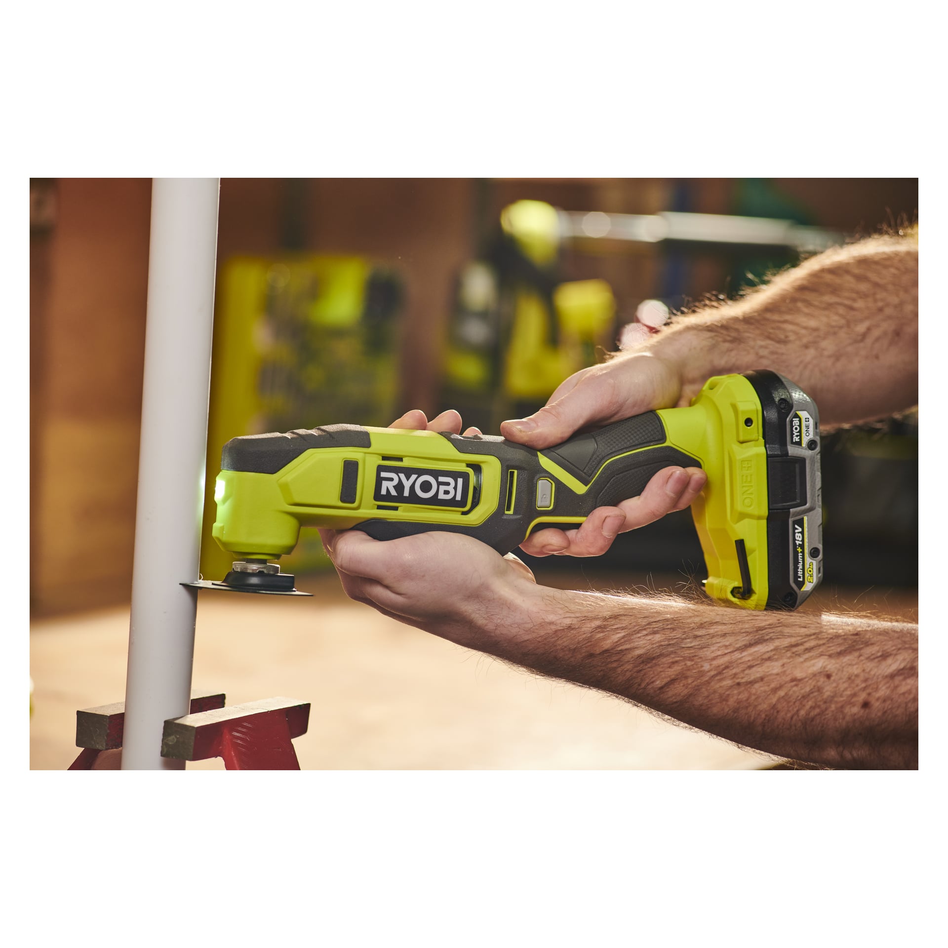 Någon använder ett Ryobi One+ Multiverktyg RMT18-0 sladdlöst oscillerande verktyg och skär av ett vitt plaströr. Användarens händer greppar säkert den gröna och svarta enheten.