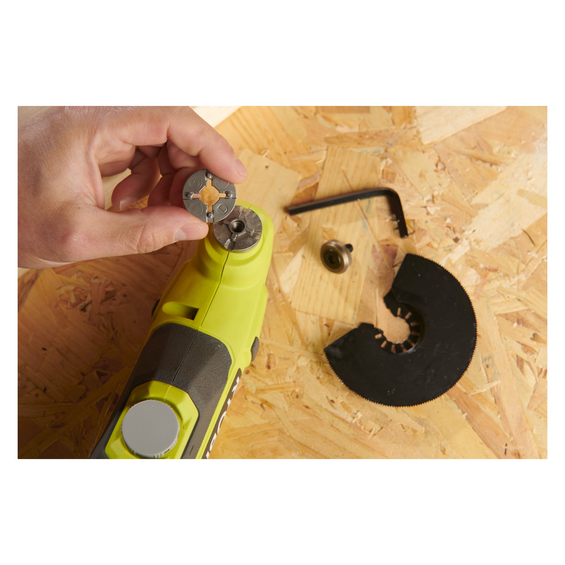 En hand håller en Ryobi One+ Multitool RMT18-0 fäste ovanför ett grönt Ryobi One+ roterande verktyg som vilar på en träyta, med en insexnyckel, skruv och svart skärblad placerade nära.
