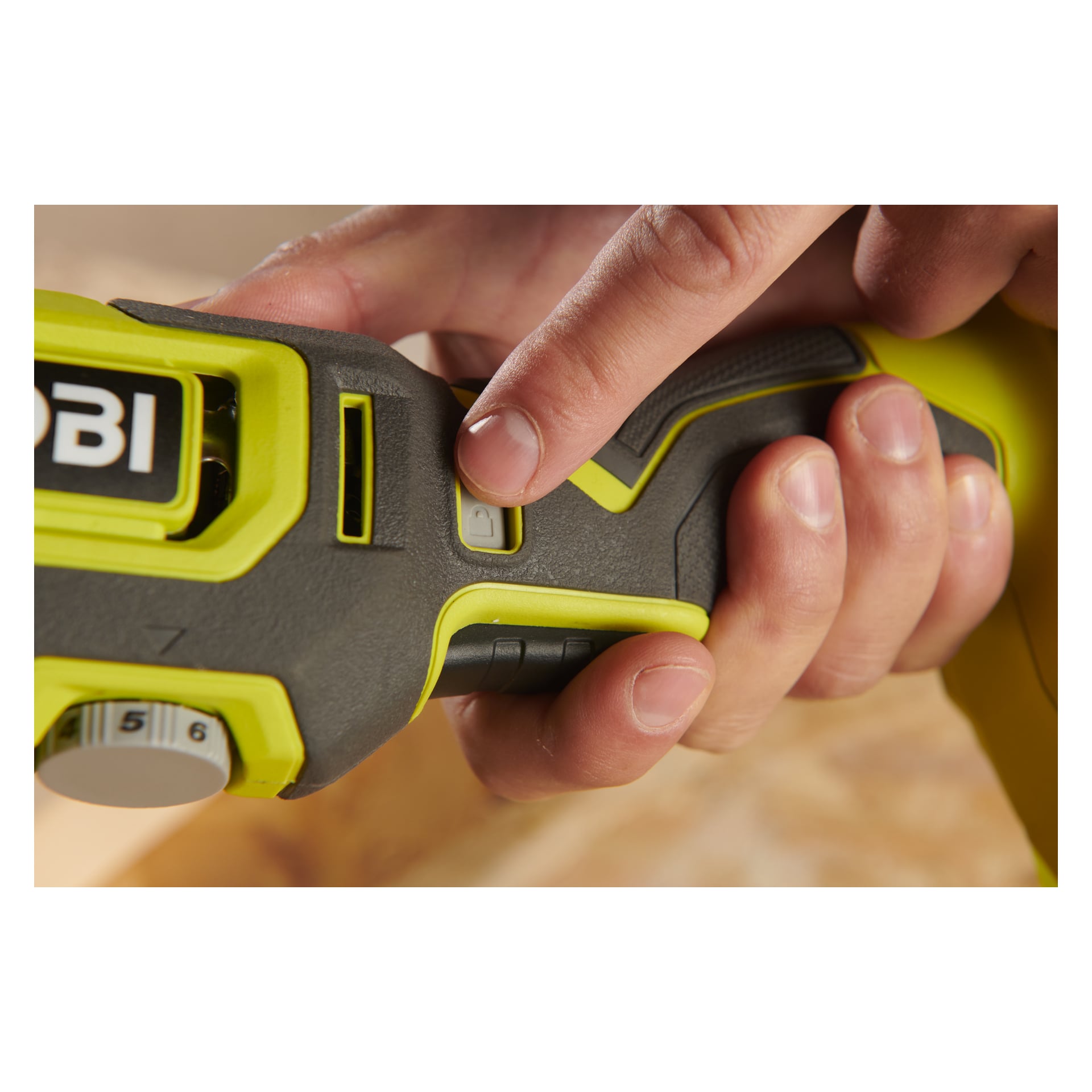 En persons hand trycker på låsknappen på handtaget på en grön och svart Ryobi One+ Multi-tool RMT18-0, vilket visar en del av verktygets logotyp och en synlig numrerad ratt.