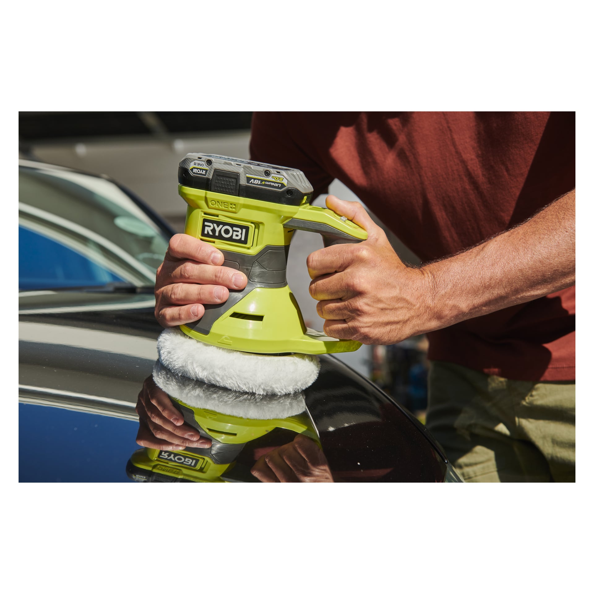 Med en röd skjorta använder man en grön Ryobi One+ Oscillating polishing machine RBP18150-0 för att polera den blanka svarta ytan på en bil, med bara armar och händer synliga.