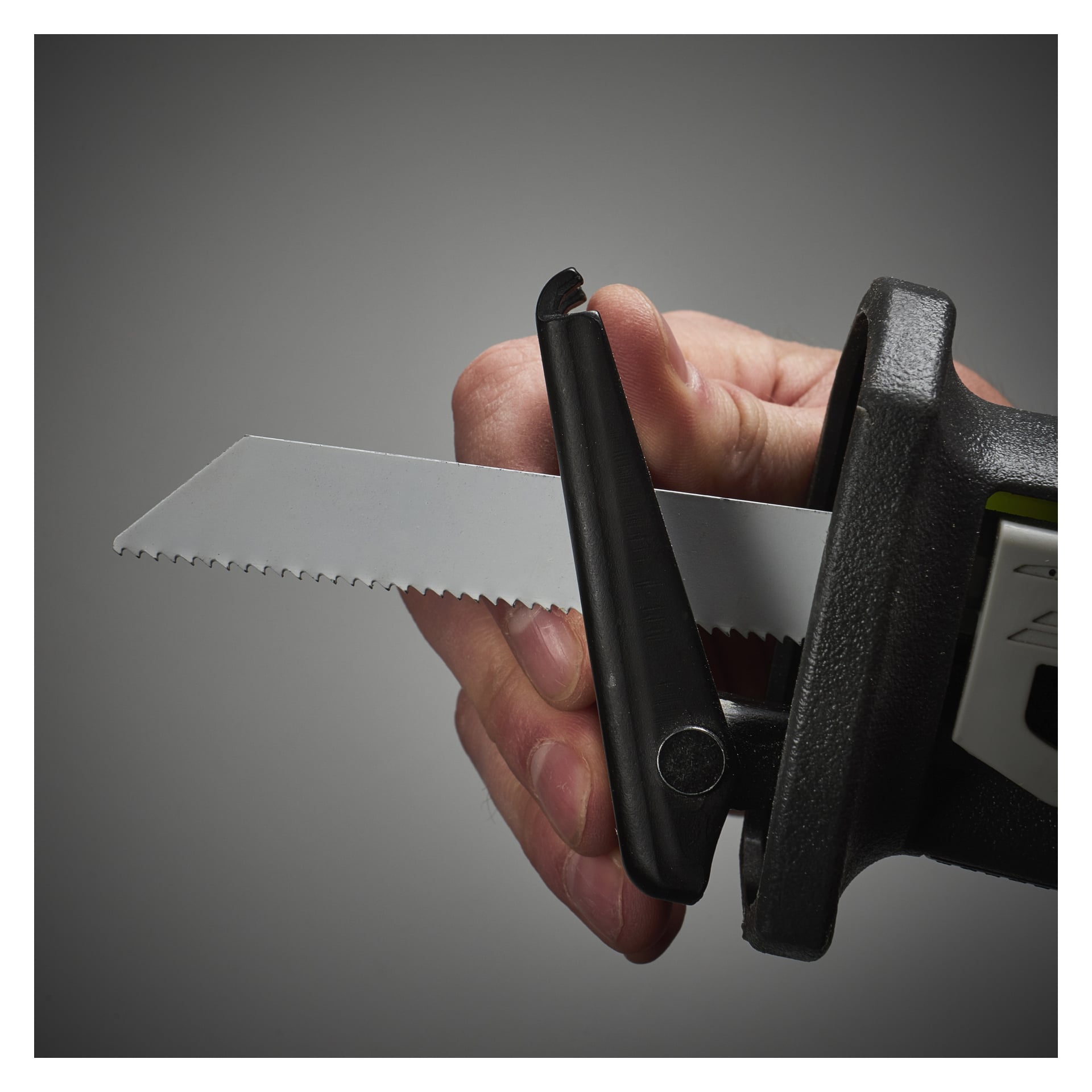 Eine detaillierte Aufnahme zeigt eine Hand, die eine gezackte Klinge an der Ryobi One+ Batterie-betriebenen Kolbensäge R18RS-0 befestigt. Sowohl die Hand als auch das Werkzeug sind scharf fokussiert, sodass die Montageschritte der Klinge klar sind.