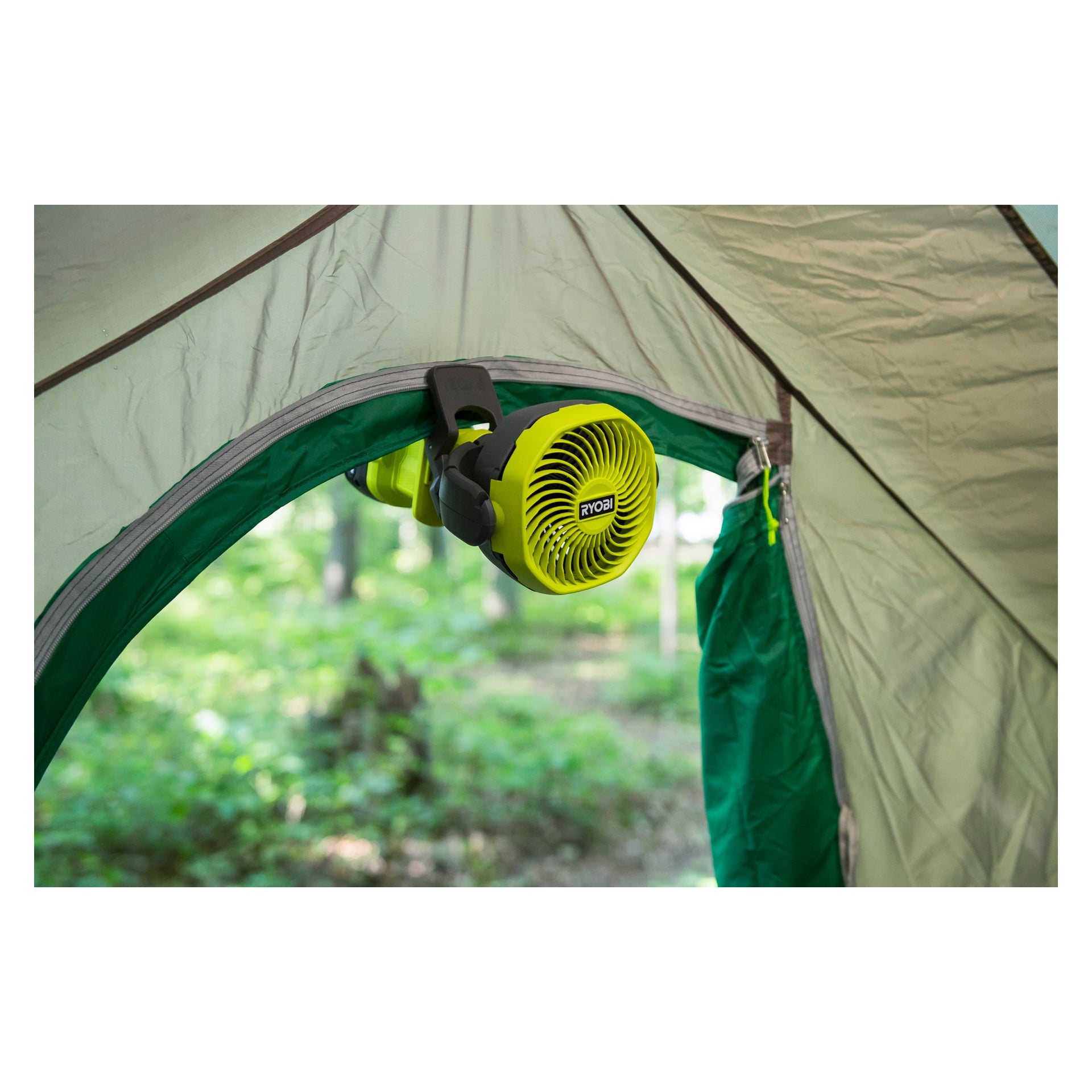 En gul Ryobi One+ batteridriven bordsfläkt (RCF18-0) är fäst vid dörrkarmen till ett grönt tält som är uppställt utomhus, med träd och frodig grönska i bakgrunden.