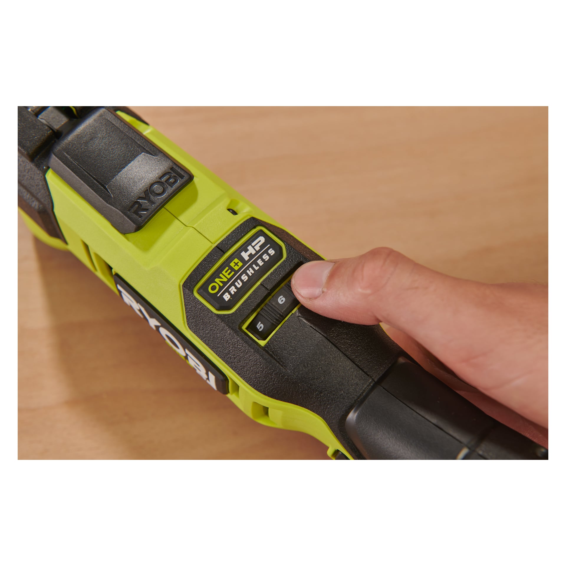 En hand trycker på knapp nummer 5 på en Ryobi One+ HP Multi-tool RMT18X-0, som har ett grönt och svart skal och vilar på en träyta.