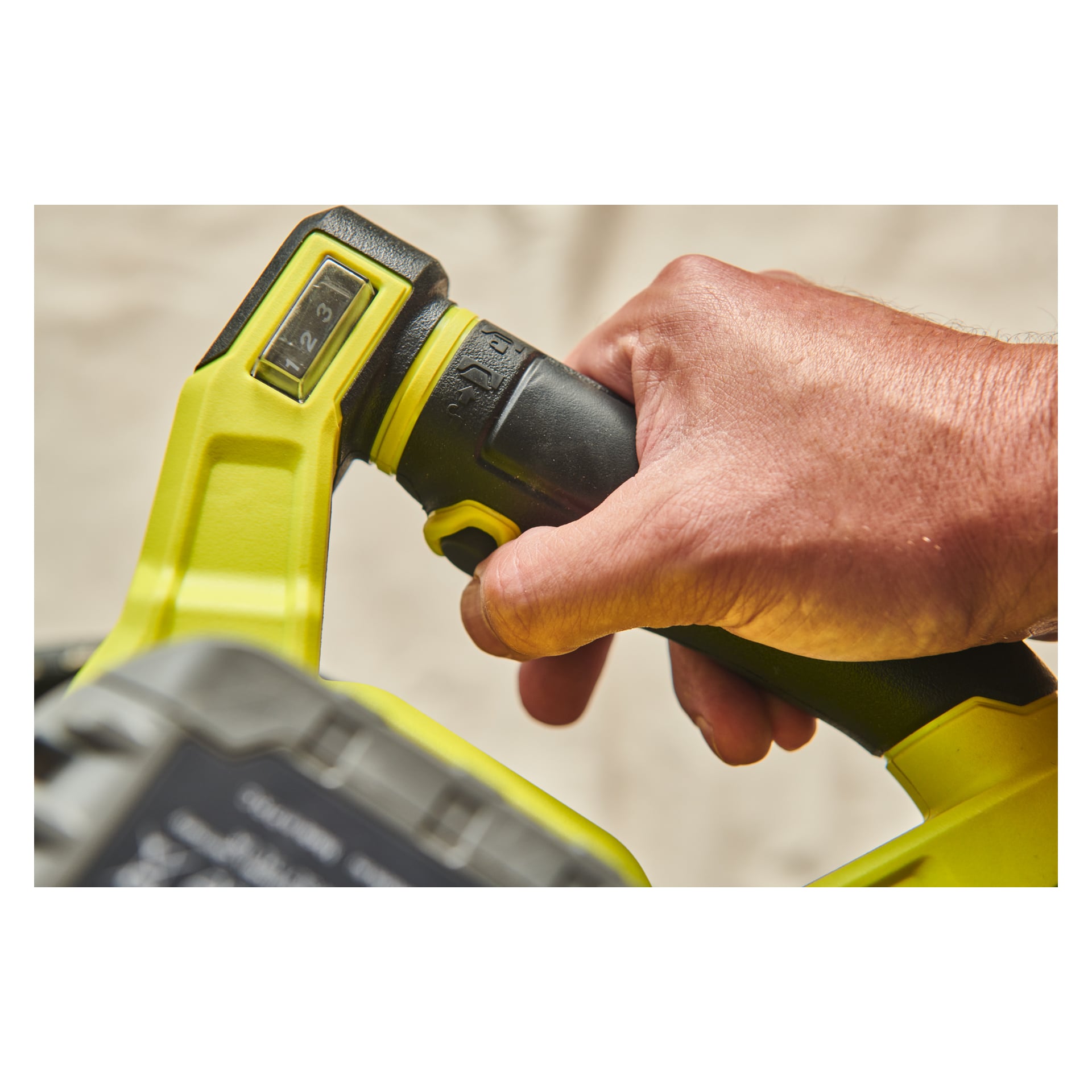 En närbild av en persons hand som håller i handtaget på en Ryobi One+ HP Agitator RPM18X-0, som har en gul och svart färgschema och en kontrollknapp med siffrorna 1 till 3 tydligt synliga.