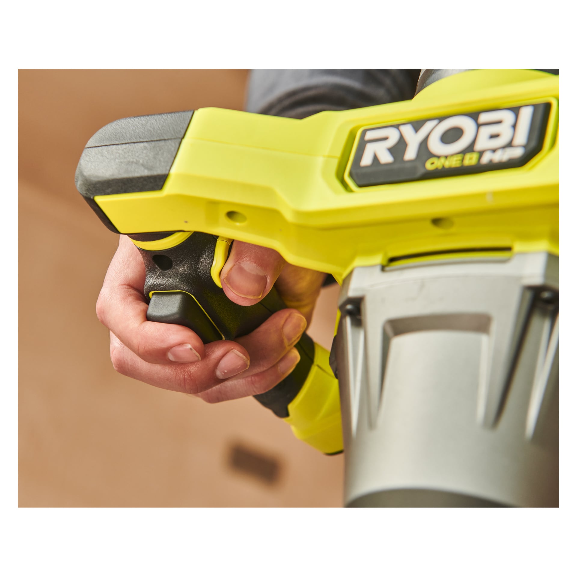 En persons hand håller hårt i handtaget på ett gult och svart Ryobi One+ HP Agitator RPM18X-0 elverktyg, vilket tydligt visar varumärket på sidan.