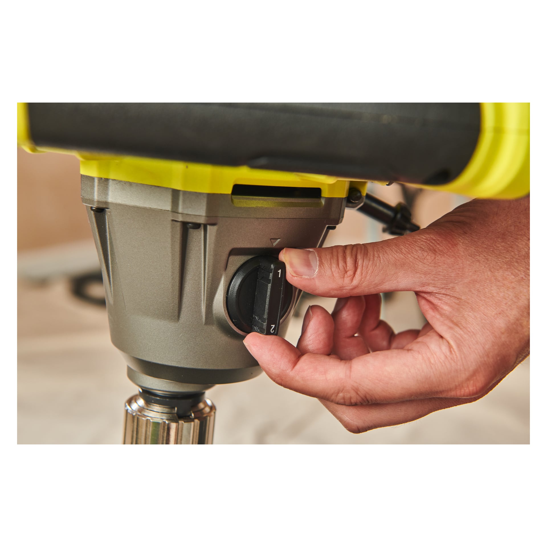 En hand justerar den numrerade ratten på ett grått och gult Ryobi One+ HP Agitator RPM18X-0 elverktyg, med bakgrunden suddig.