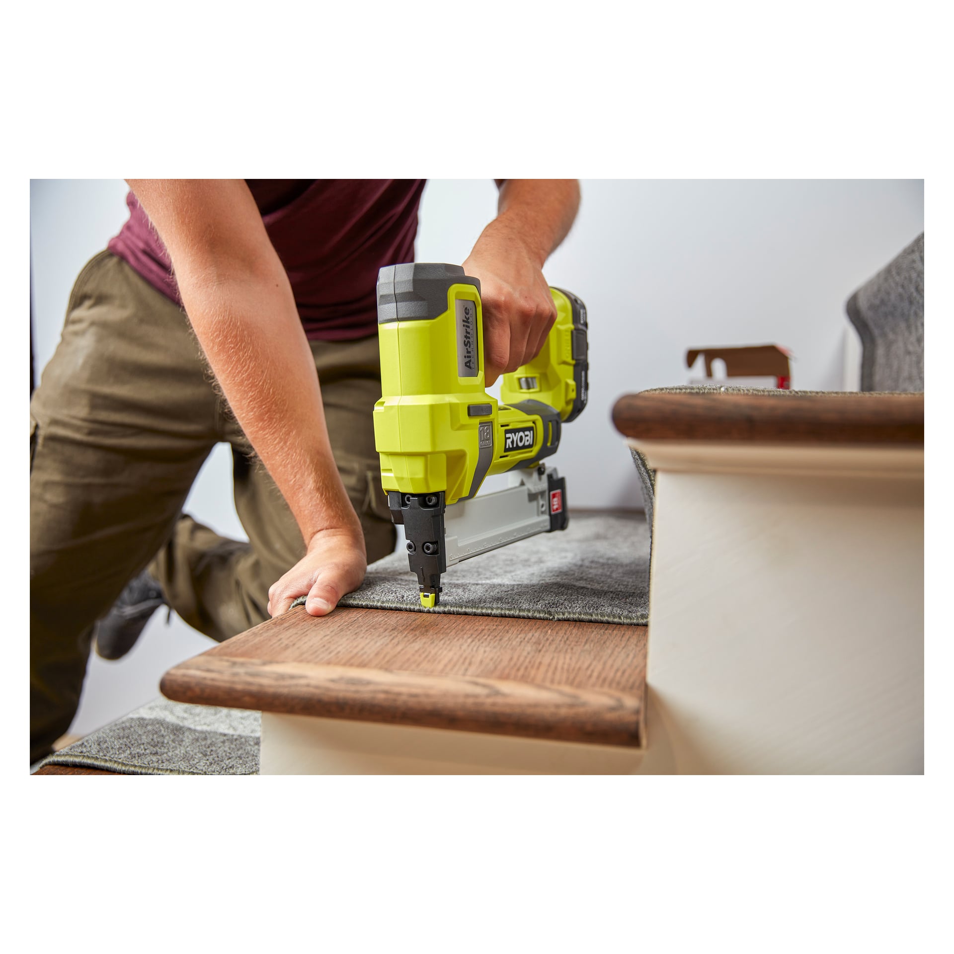 En person knäböjer på ett knä medan han fäster mattan på en trätrappa med Ryobi One+ Staple Gun R18GS18-0, och trycker ner mattan med vänster hand.