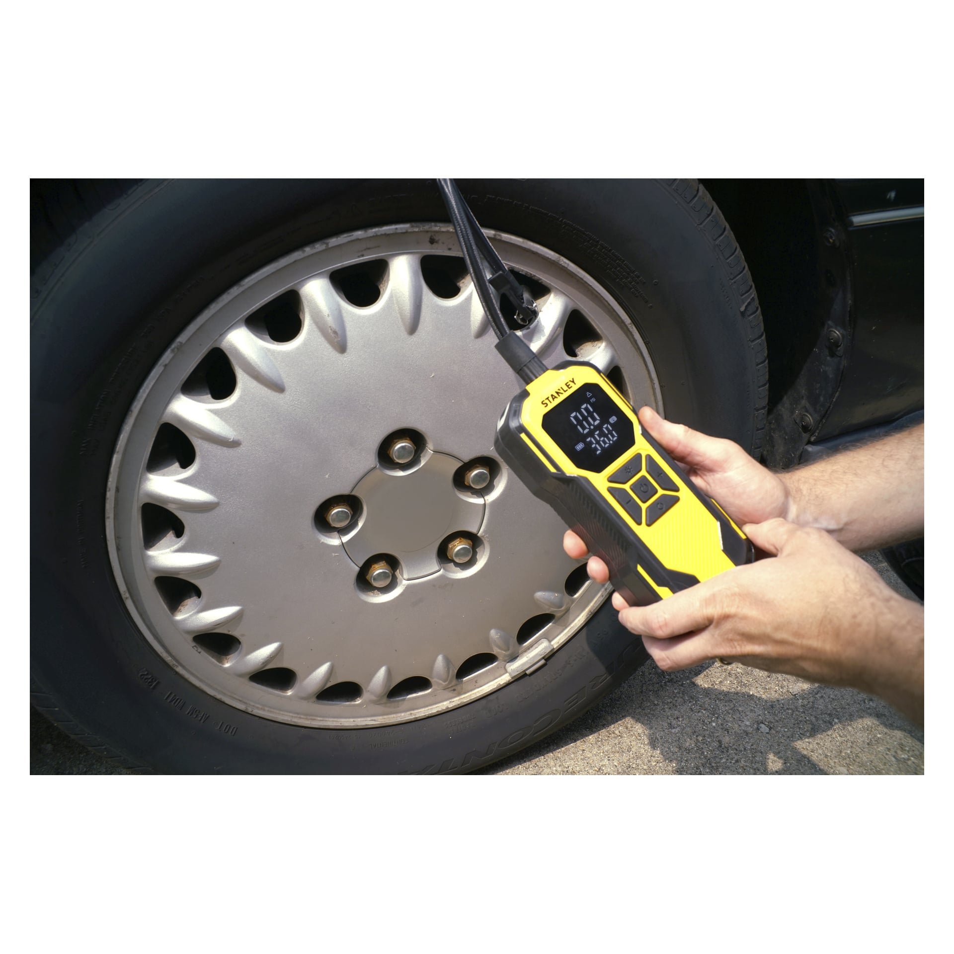 Ktoś używa samonaładowanej mini pompy powietrznej Stanley Rechargeable Mini SXIF0101 na trzpieniu zaworów opony samochodowej. Na ekranie widać 32,0 PSI, a opona ma srebrną pokrywkę z sześcioma nakrętkami na śrubach.