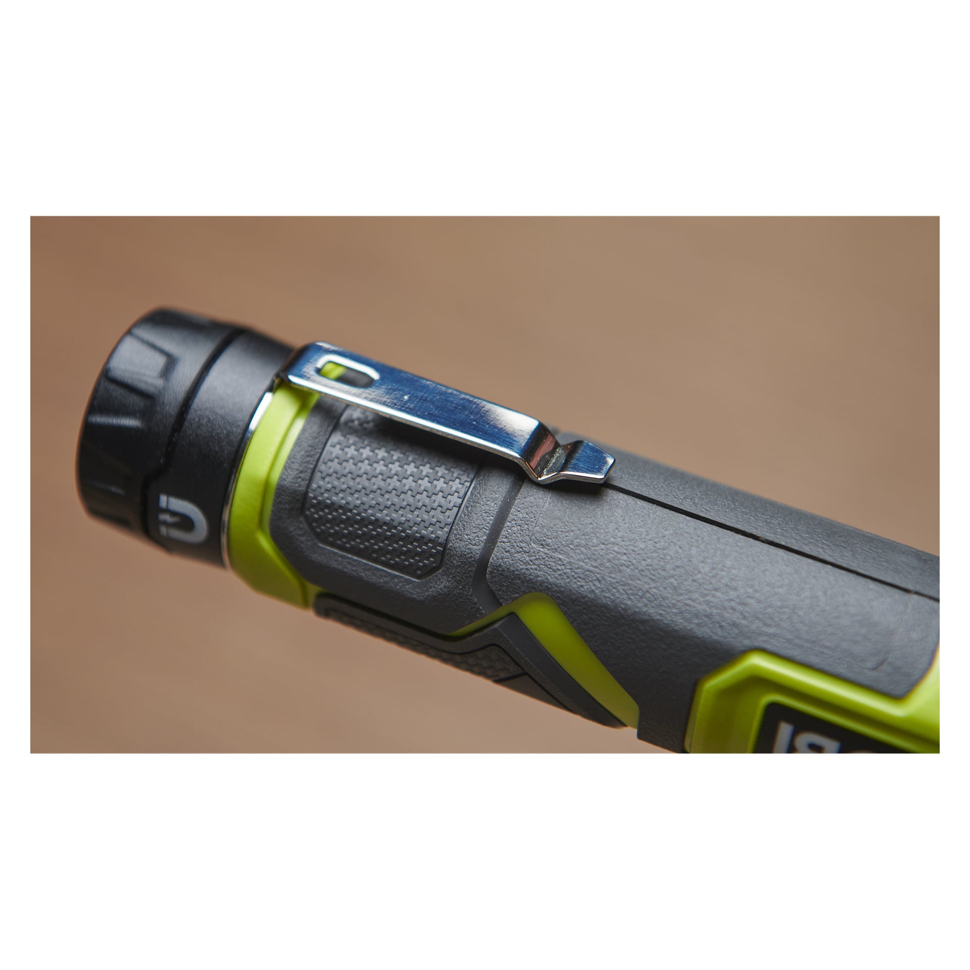Detaljerad vy av en Ryobi USB Lithium Work lampa RLI4-0, som visar en grå och grön handhållen enhet med ett texturerat grepp, metallfickklämma och framträdande strömknapp i ena änden.