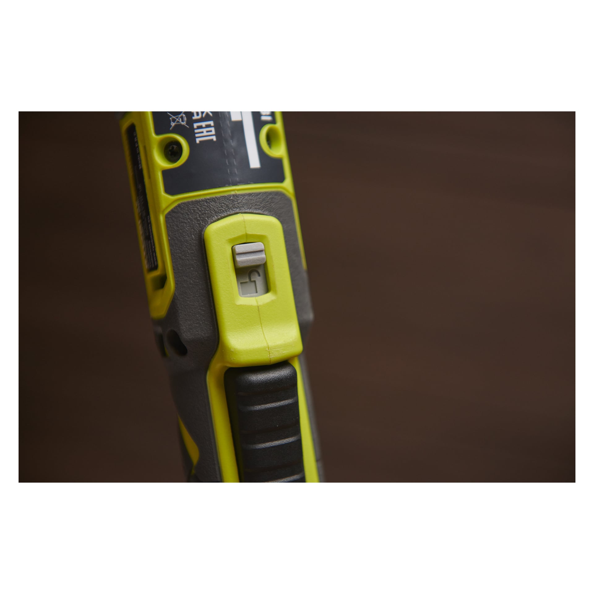 En närbild av Ryobi USB Lithium Battery-drivna spärrnyckeln RR14W4-0 har ett gult och grått handtag med en vit strömbrytare i mitten, mot en suddig brun bakgrund.