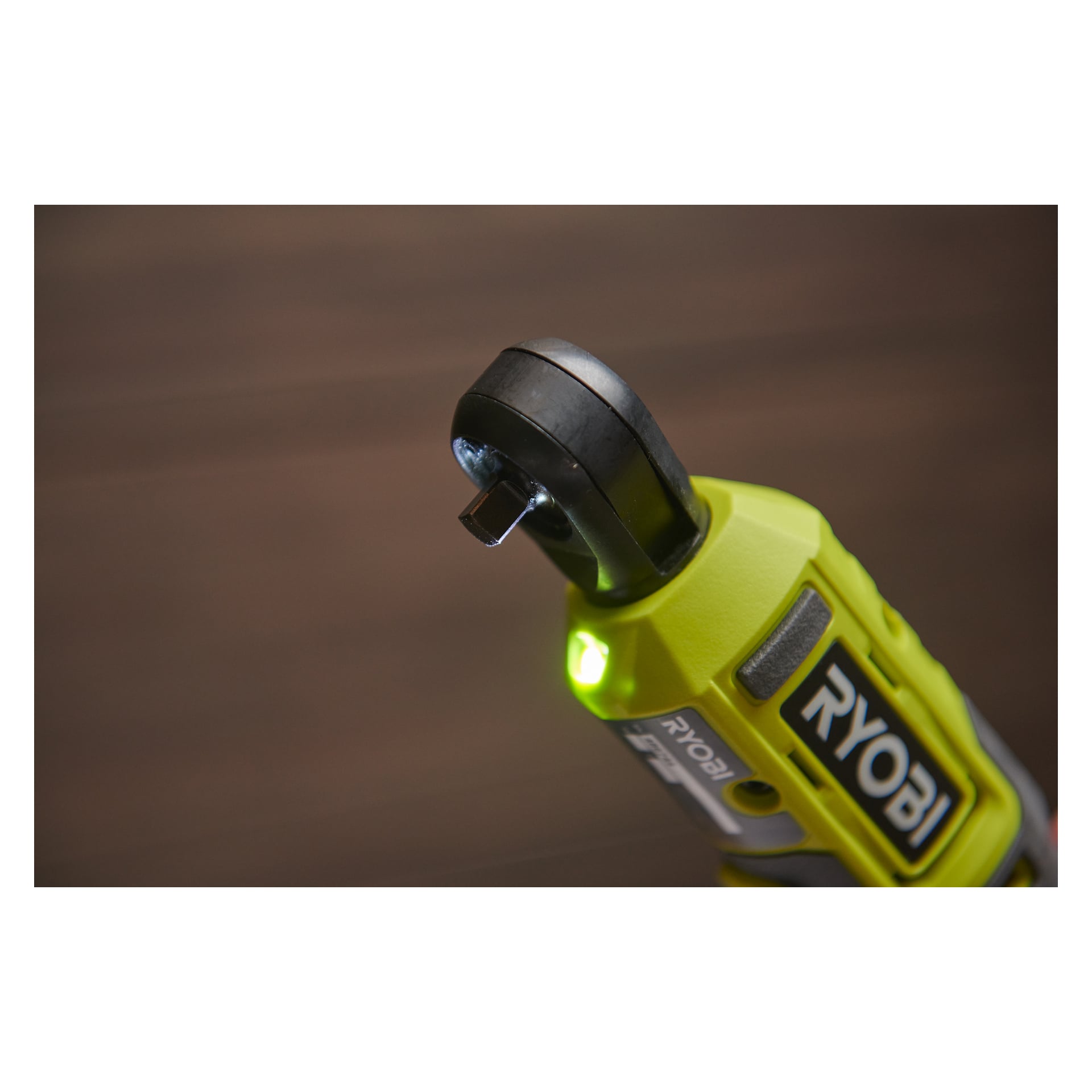 Närbild av huvudet på en Ryobi USB Lithium batteridriven spärrnyckel RR14W4-0, med varumärkesloggan, en del av handtaget och den fyrkantiga drivenheten. Ett grönt indikatorljus lyser på verktyget, med en suddig bakgrund.