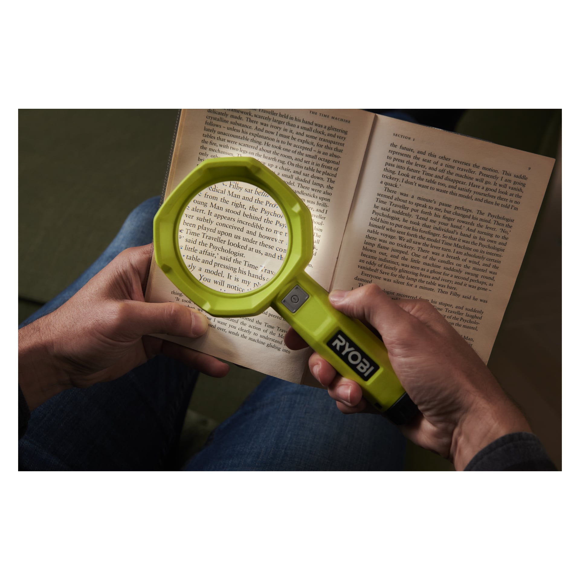 En person använder Ryobi USB Litiumförstoringsglas med lampa RML4-0 för att förstora en del av en öppen bok, med båda händerna synliga, vilket markerar enheten och den förstorade texten.