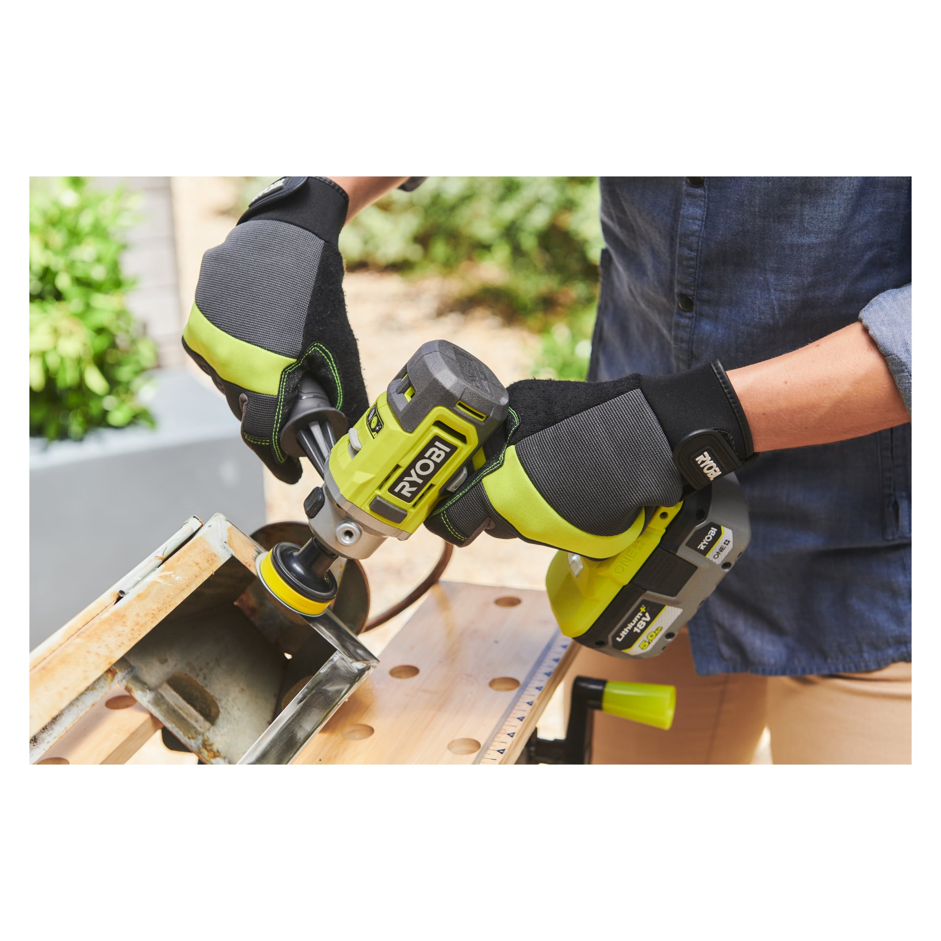 Med svarta och gröna handskar använder man ett Ryobi One+ Polisher/detaljslipare RDP18-0 sladdlöst elverktyg för att slipa eller polera ett metallföremål på en träarbetsbänk utomhus.