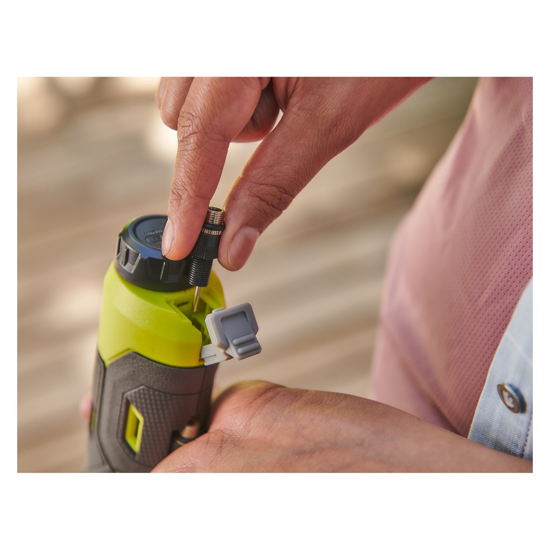 Noen fester en svart ventil til en grønn og grå Ryobi USB Lithium mini-kompressor RI4-120G, og holder den stødig med én hånd.