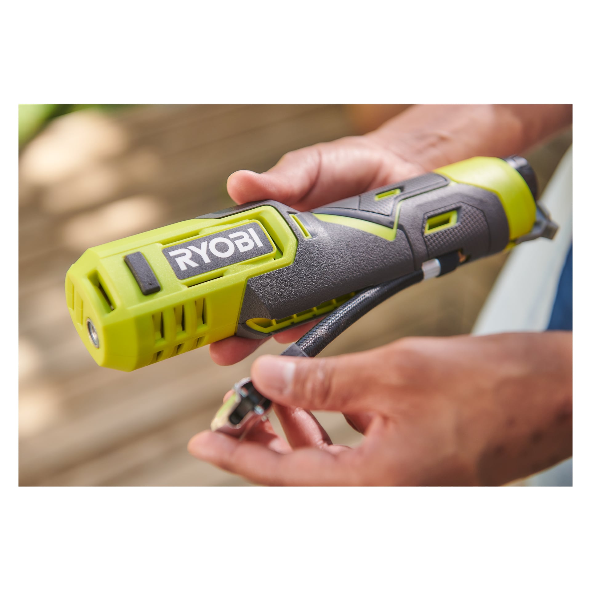 En person holder en svart og grønn Ryobi USB Lithium mini-kompressor RI4-120G, som viser dysen og slangefestet.