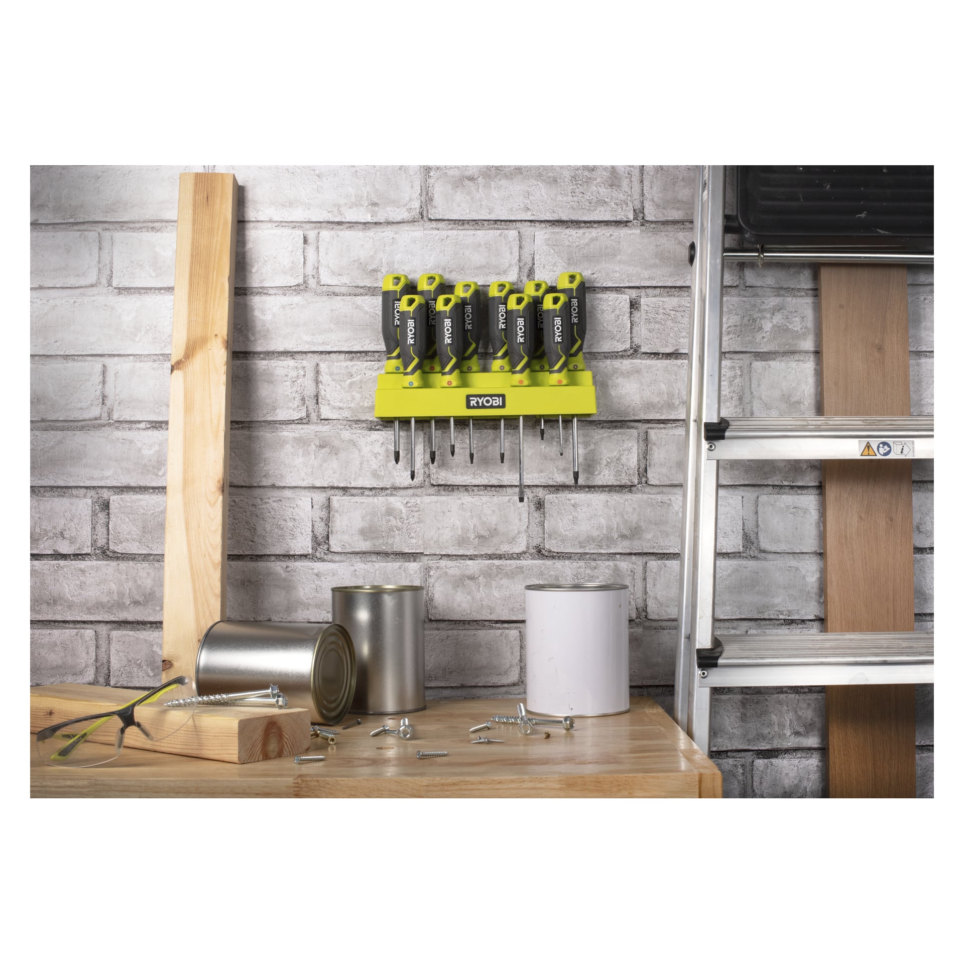 Ryobi RHSDS10PCP 10-teiligen Schraubendreher an einer grauen Backsteinwand über einer Werkbank mit Dosen, Schrauben und Holzstücken; Leiter rechts.