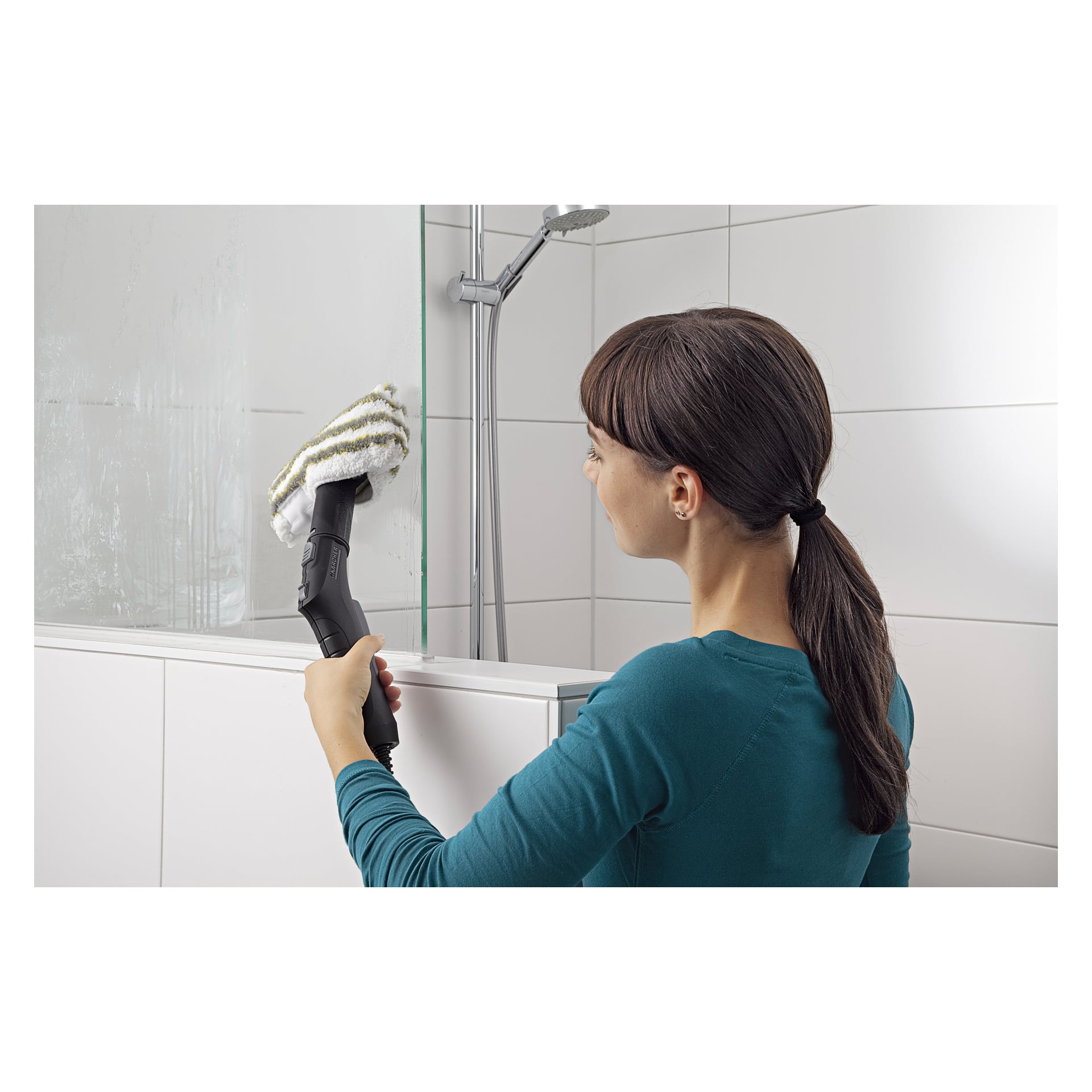 En kvinna i en tealfärgad skjorta ångrengör en glasduschdörr i ett vitkaklat badrum med hjälp av Kärcher Cleaning Cloths (set om 4).