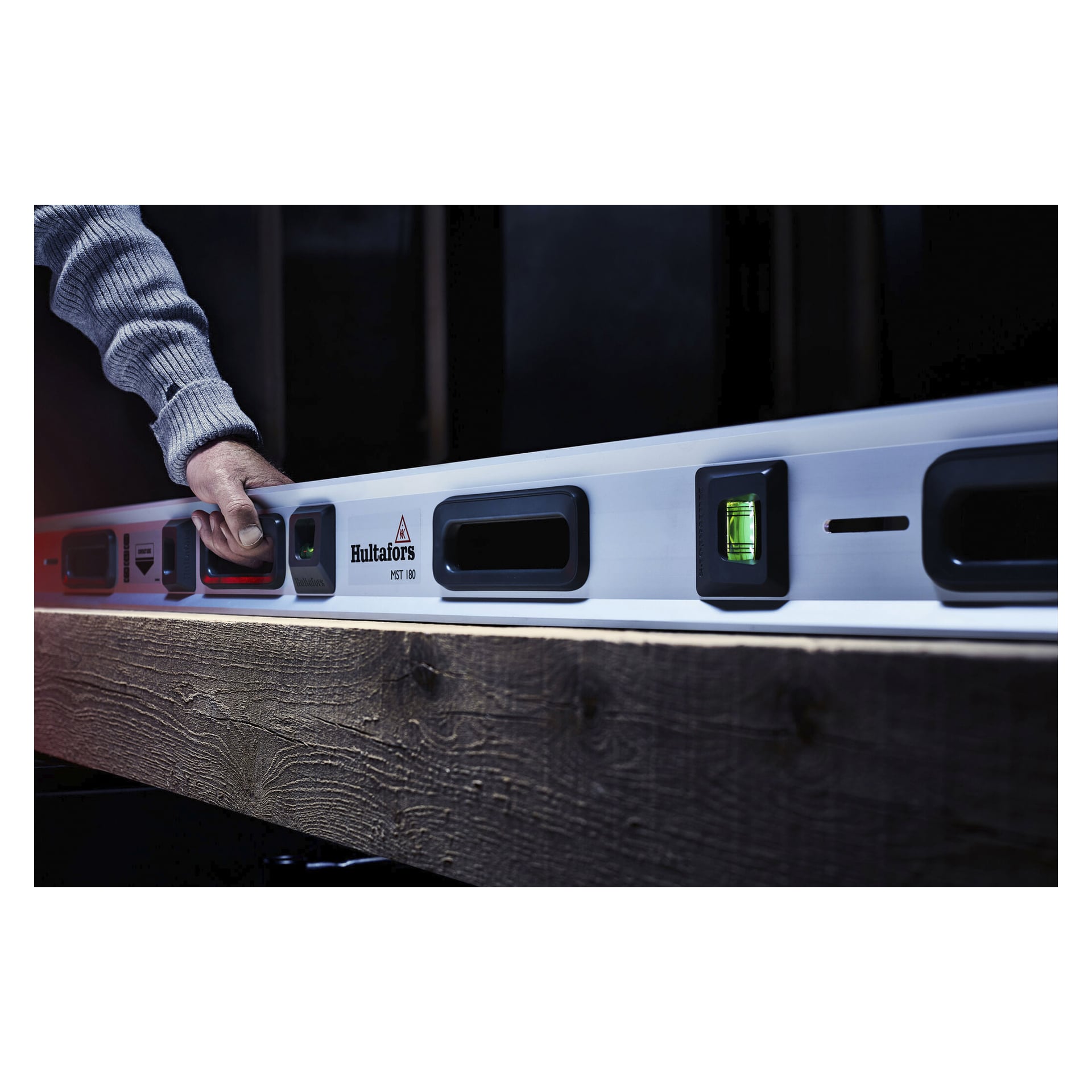 En hand justerar Hultafors MST digitala vattenvater på en träbalk, och visar tända flaskor och kontrollknappar på verktyget.