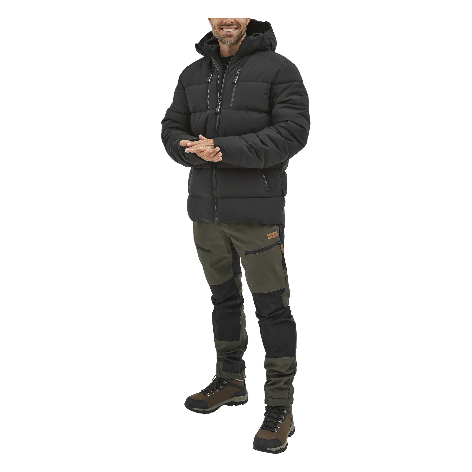 Leende knäpper en person i Kayoba Outdoor herrskängor, svart dunjacka och mörkgrön-svarta cargobyxor sina händer.