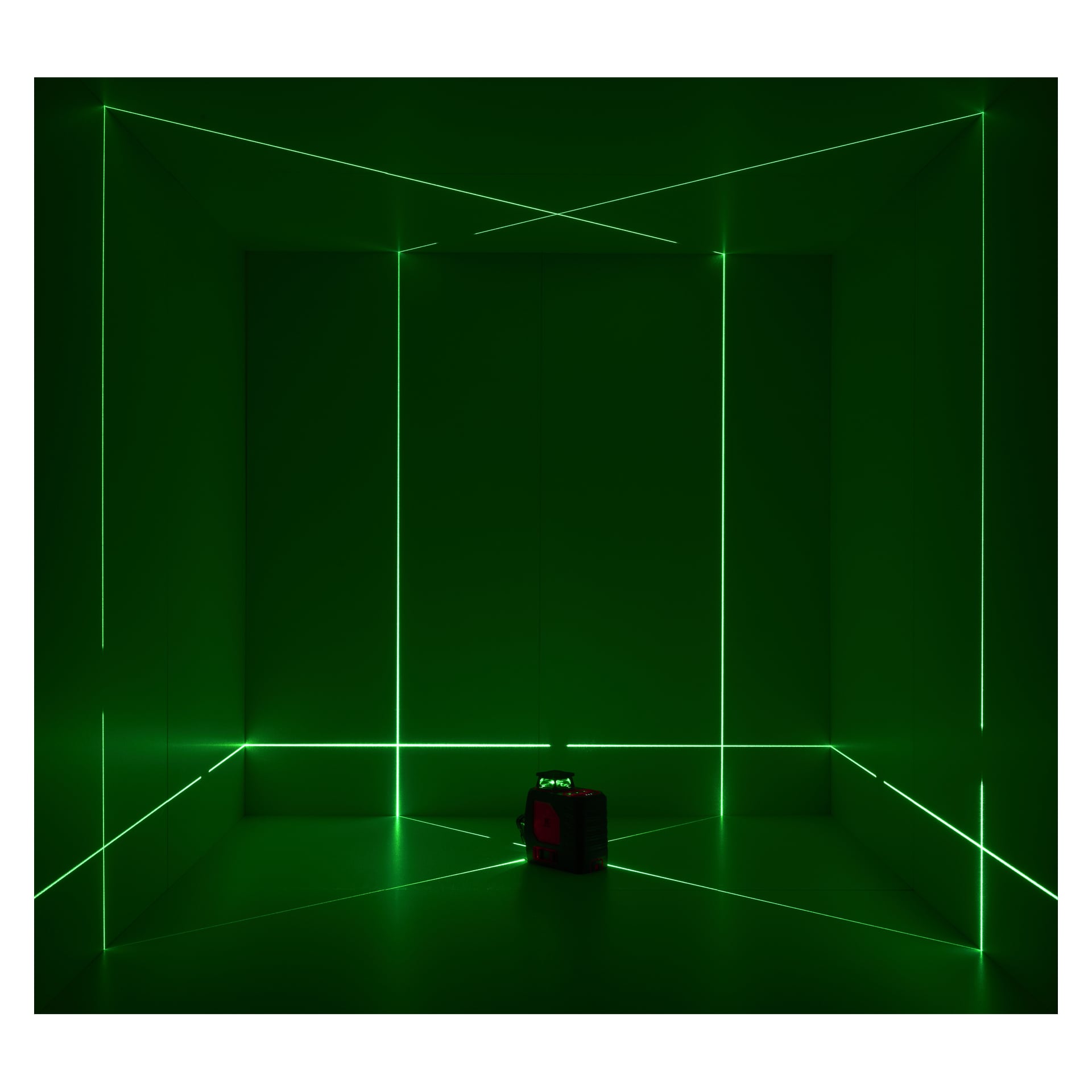 Geometriske grønne laserlinjer fra en Meec Tools Crosshair-laser lyser opp et mørkt rom, enheten sentrert på gulvet.