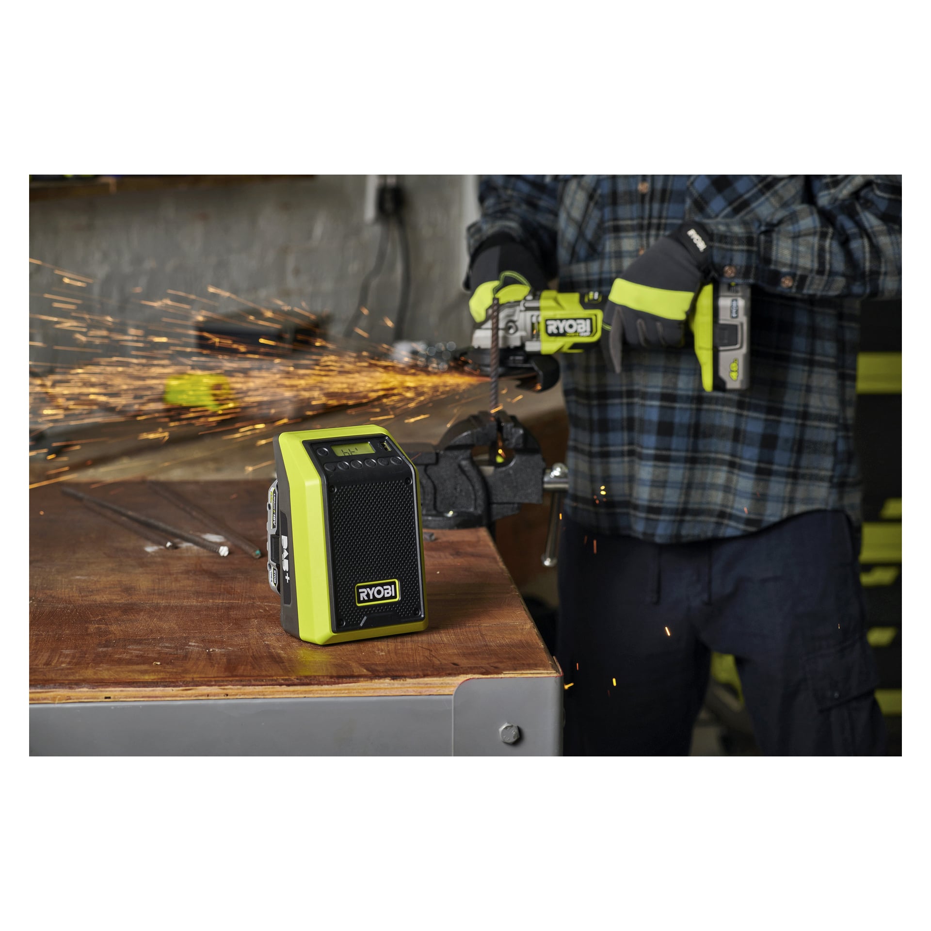 Handskbeklädda händer manövrerar en Ryobi-vinkelslip på metall, gnistor flyger; en Ryobi One+ Bluetooth-högtalare står på arbetsbänken i närheten.