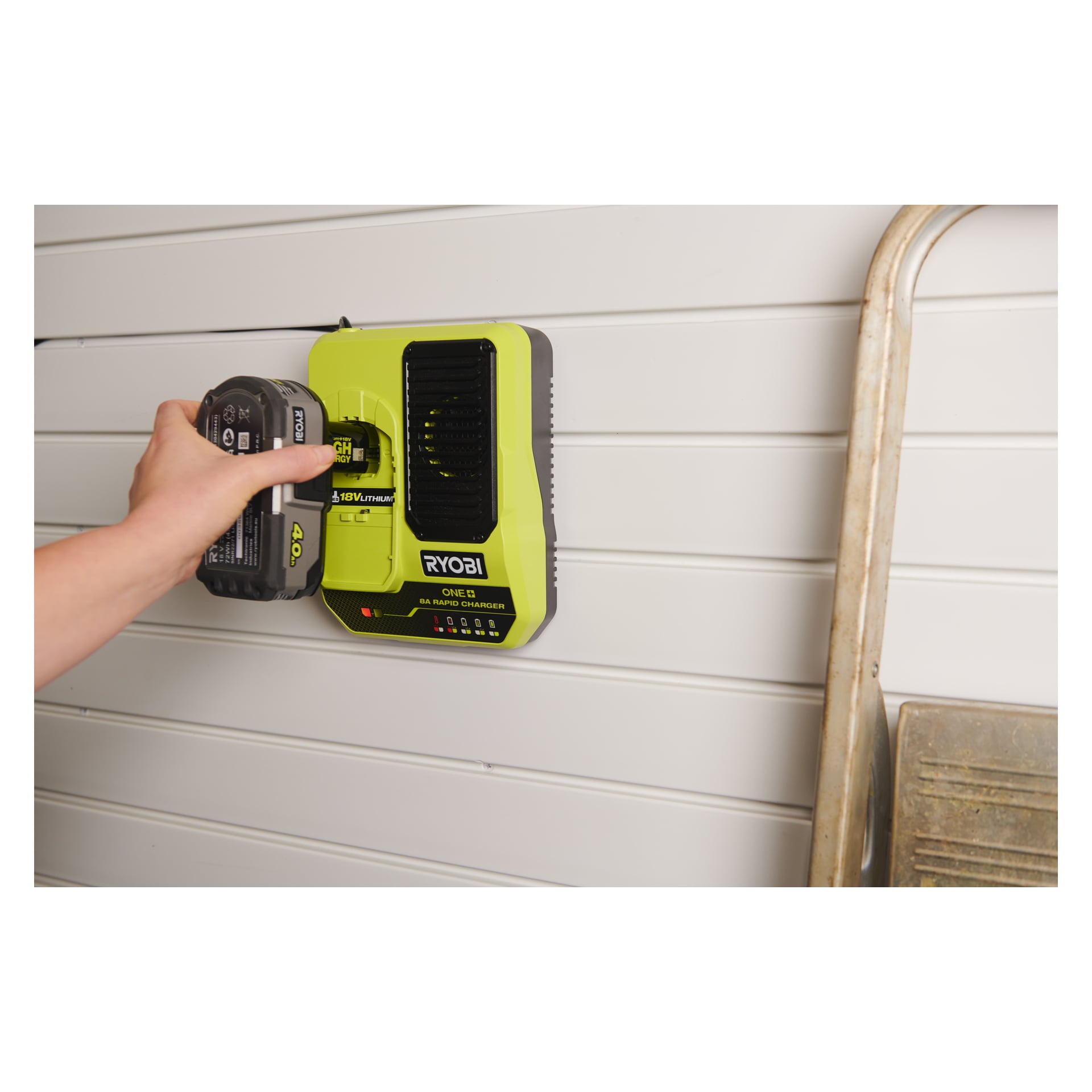 En hand placerar en Ryobi One+ Quick-laddare RC18180 40V-batteri i en väggmonterad snabbladdare; Metallstege delvis synlig till höger.