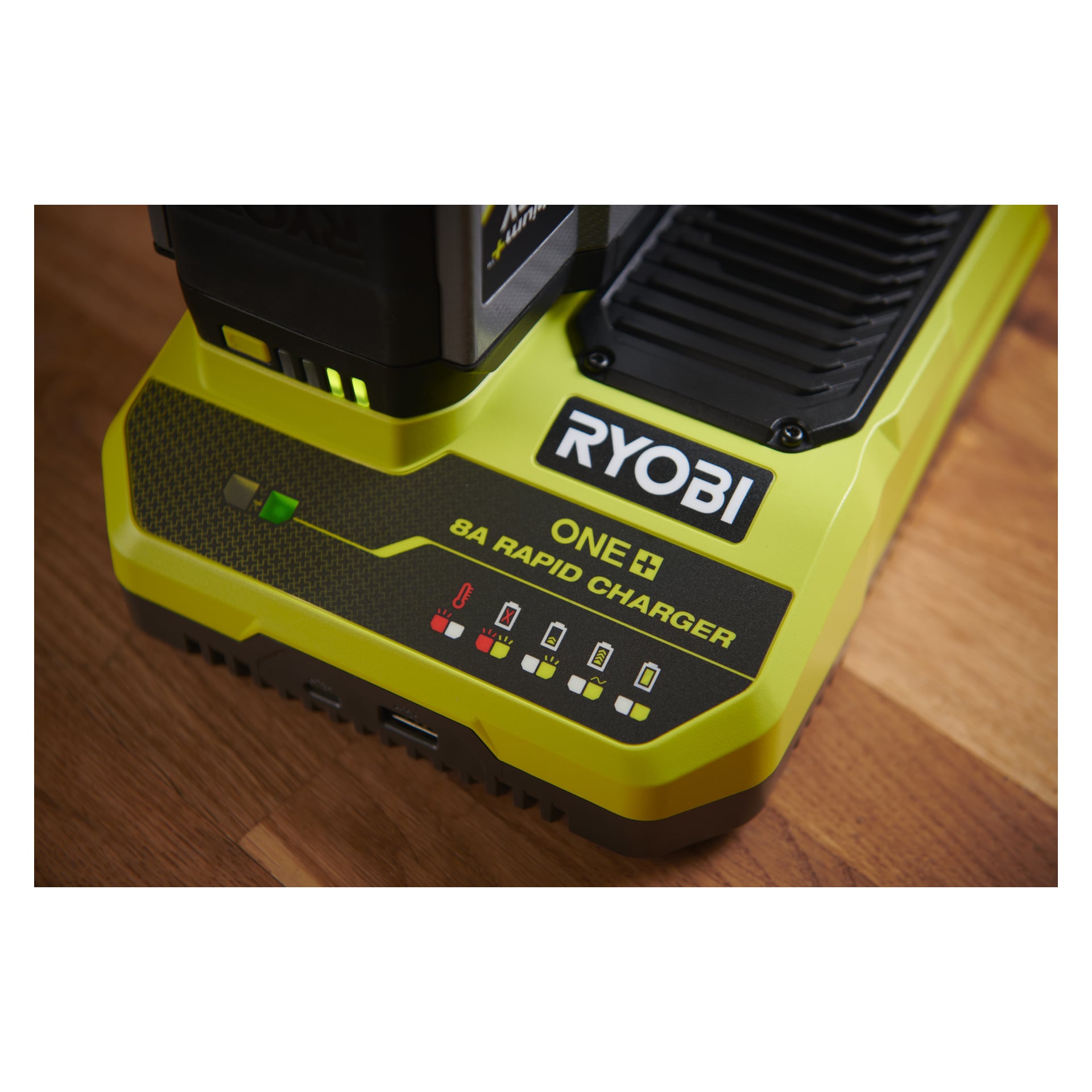 Närbild på en Ryobi One+ Quick Charger RC18180 på trä, med indikatorlampor, varumärkeslogga och ett delvis insatta batteri.