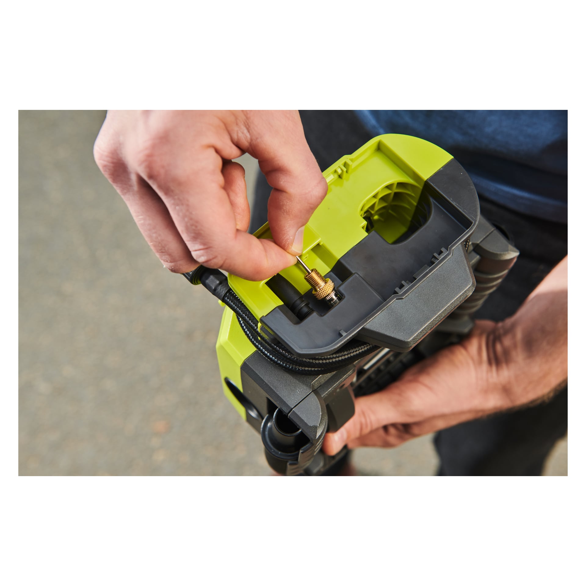 Händerna kopplar en mässingsventil till en Ryobi One+ batteriluftkompressor RMI18-0, med dess spiralspolade slang synlig.