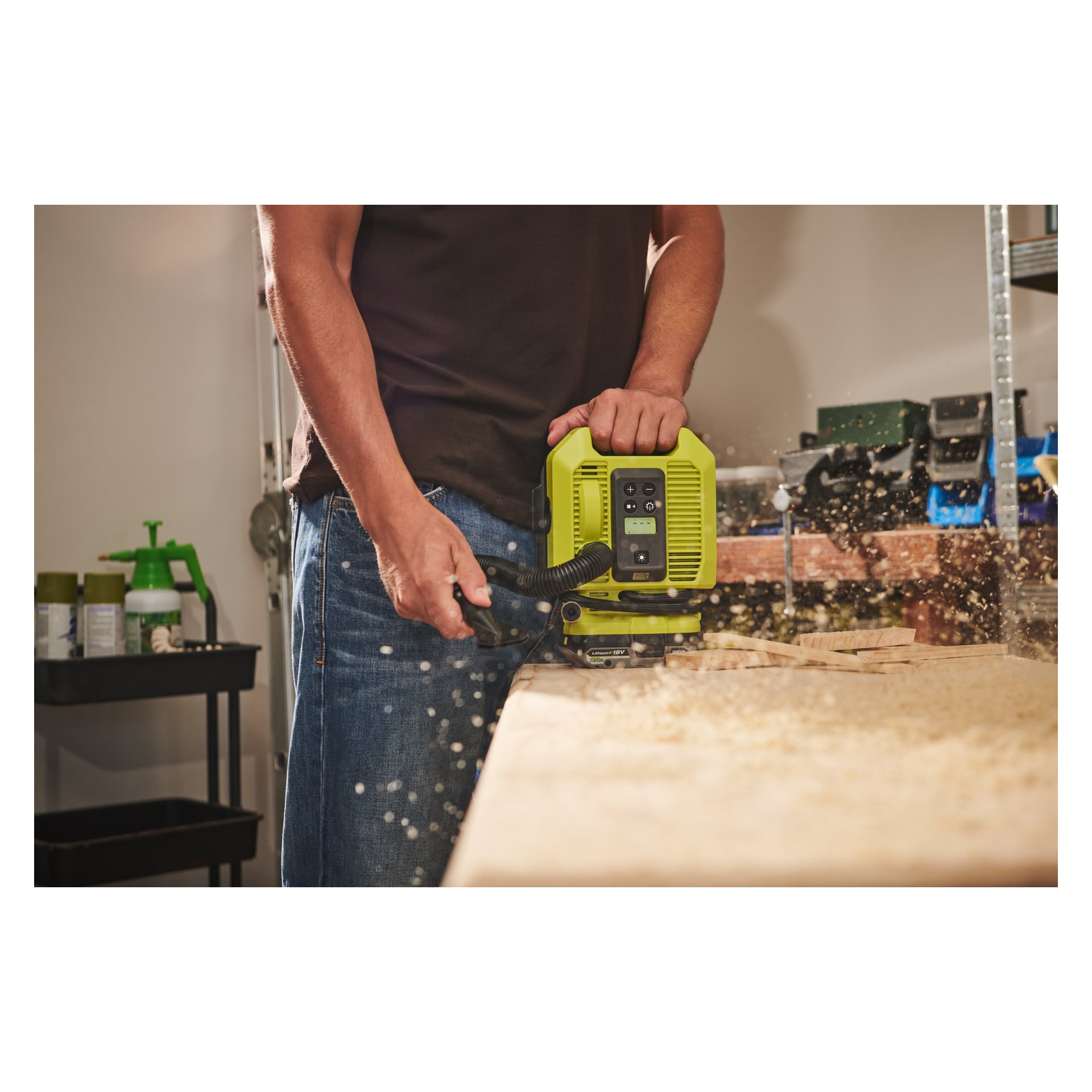 Någon använder en Ryobi One+ RMI18-0 batteriluftkompressor vid en arbetsbänk, omgiven av olika verktyg och förnödenheter.