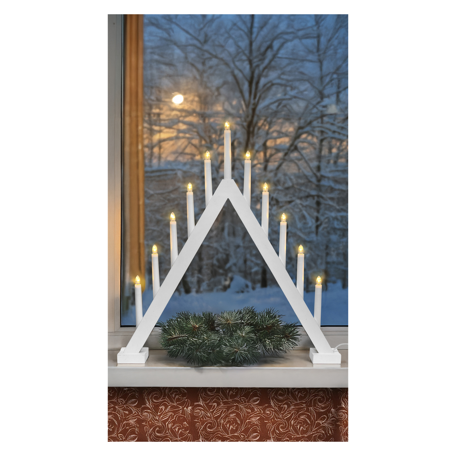 Ein weißer dreieckiger EKVIP Large LED Adventskerzenhalter mit neun leuchtenden Kerzen auf einem Fensterbrett, Kiefernäste, verschneite Bäume, Sonnenuntergang.