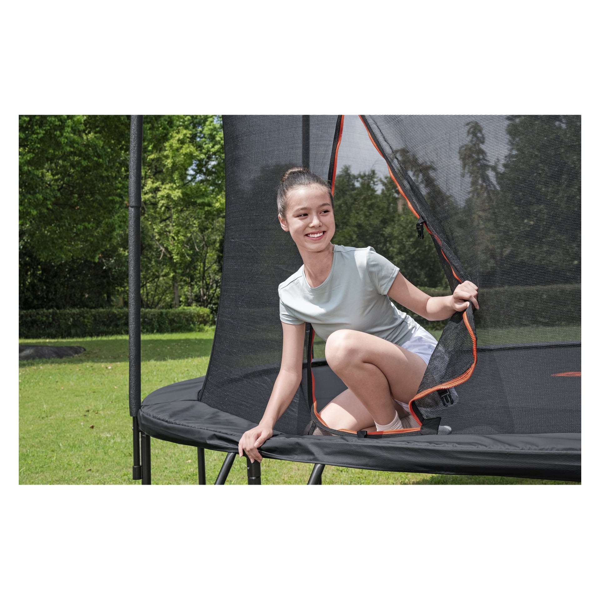 En ung person klatrer gjennom glidelåsinngangen på en Bestway Xtreme Air Trampoline 59120, satt opp på gress med trær bak.