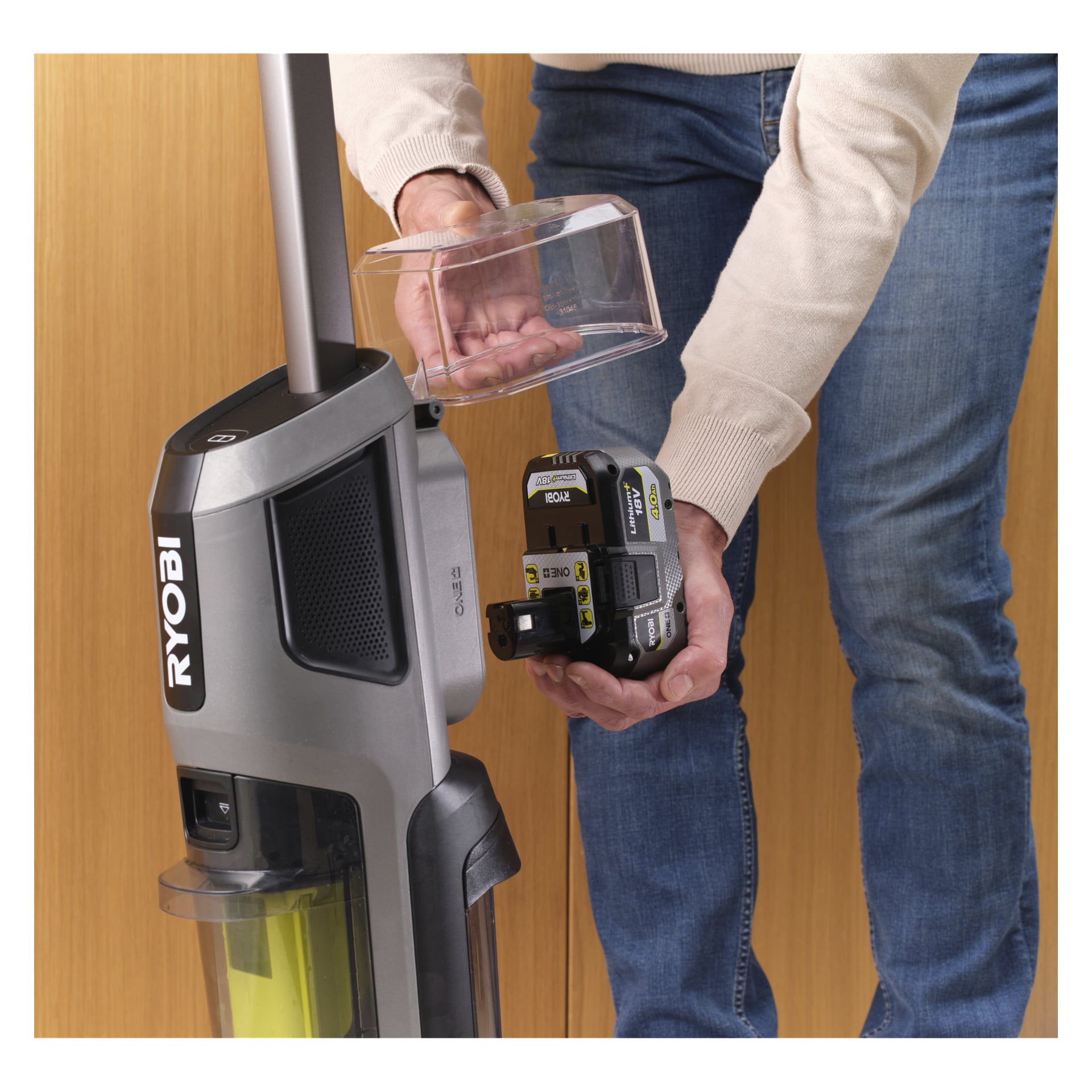 Någon placerar ett Ryobi One+ 18V-batteri i en upprätt 3-i-1-dammsugare med moppfunktion, placerad bredvid en träyta.