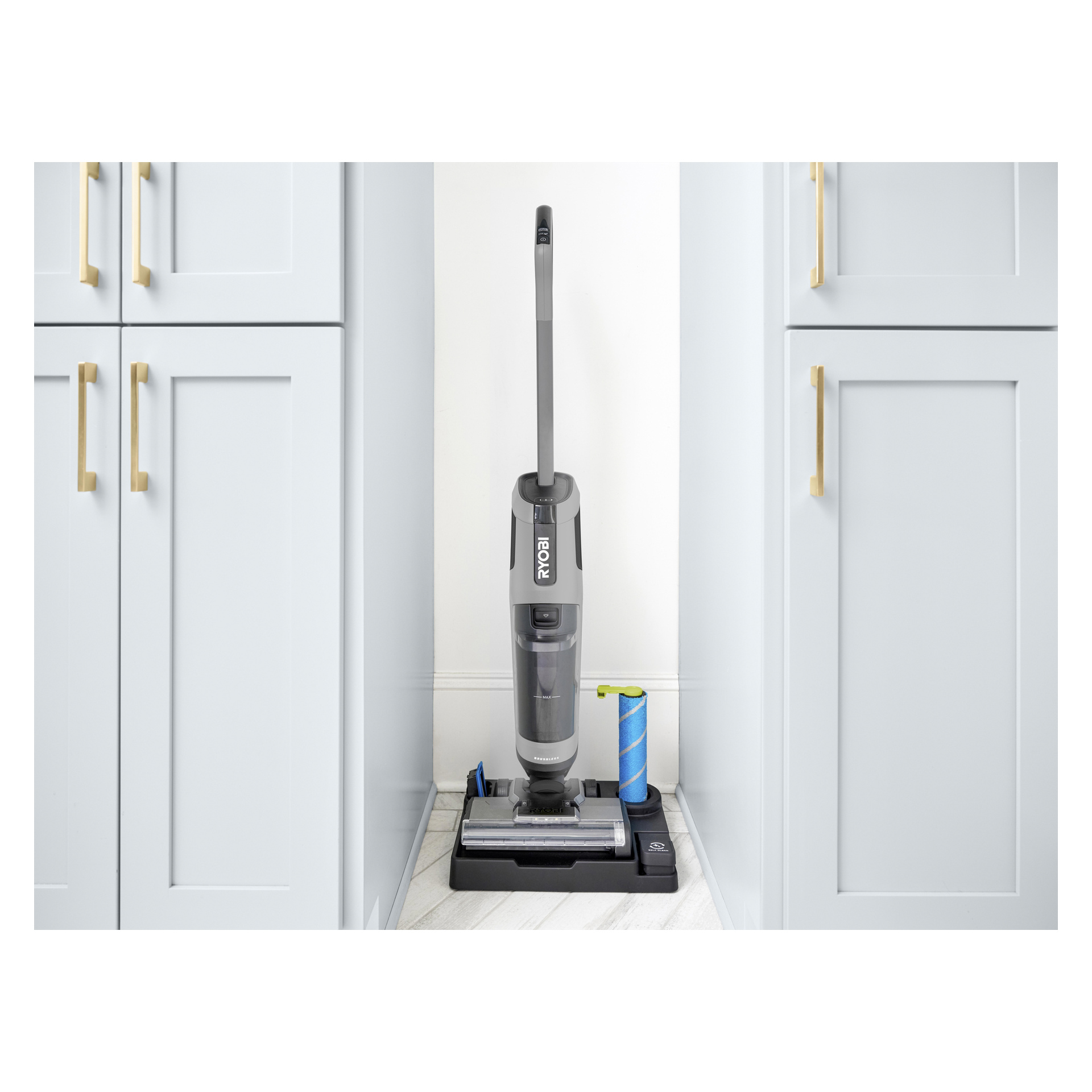 En Ryobi One+ 3-i-1 stående dammsugare med moppställ laddad i en vit nisch mellan grå skåp, rullfäste bredvid.
