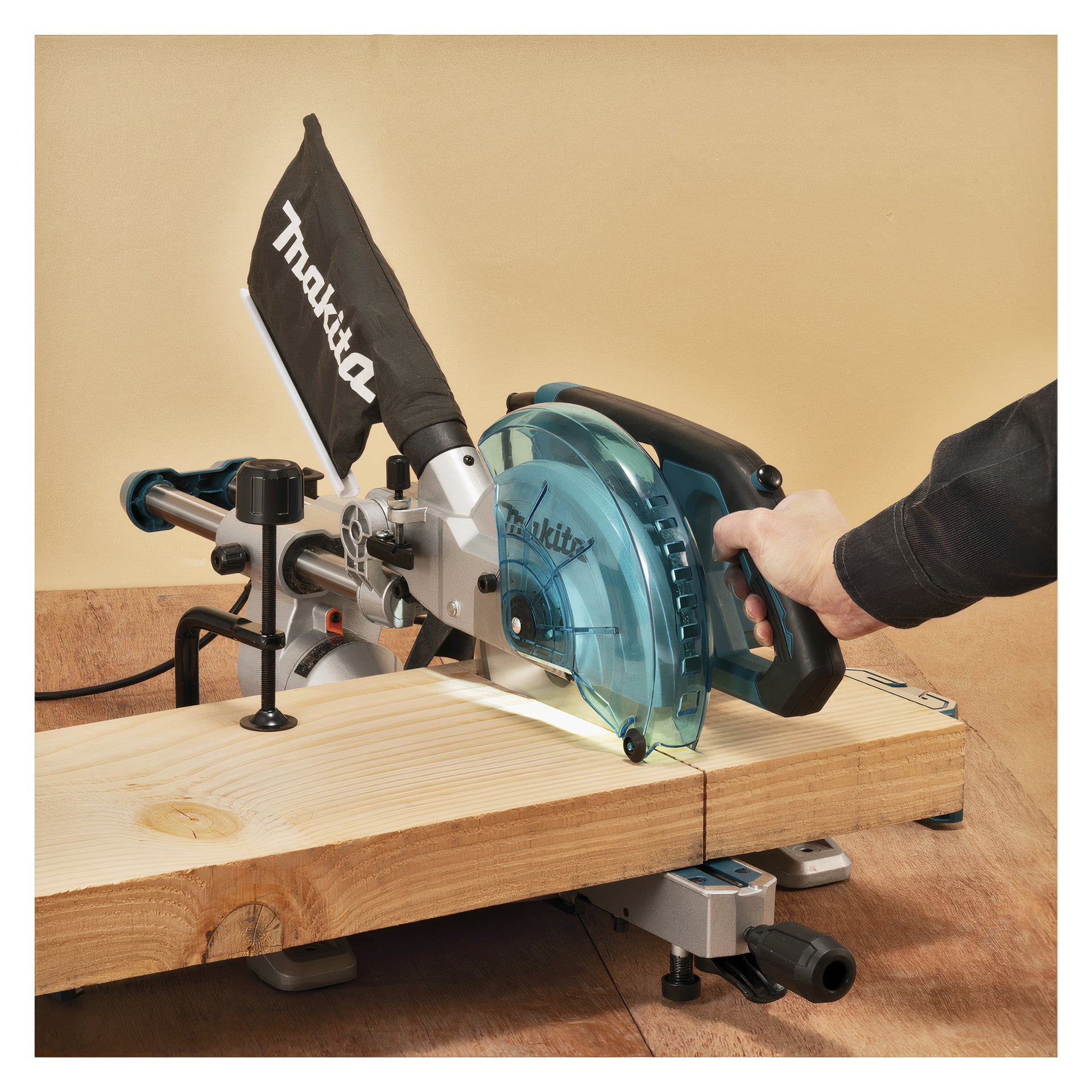 Noen bruker en Makita LS0816F gjærsag, med støvpose og blå bladbeskyttelse, for å kutte en treplate på en arbeidsbenk.