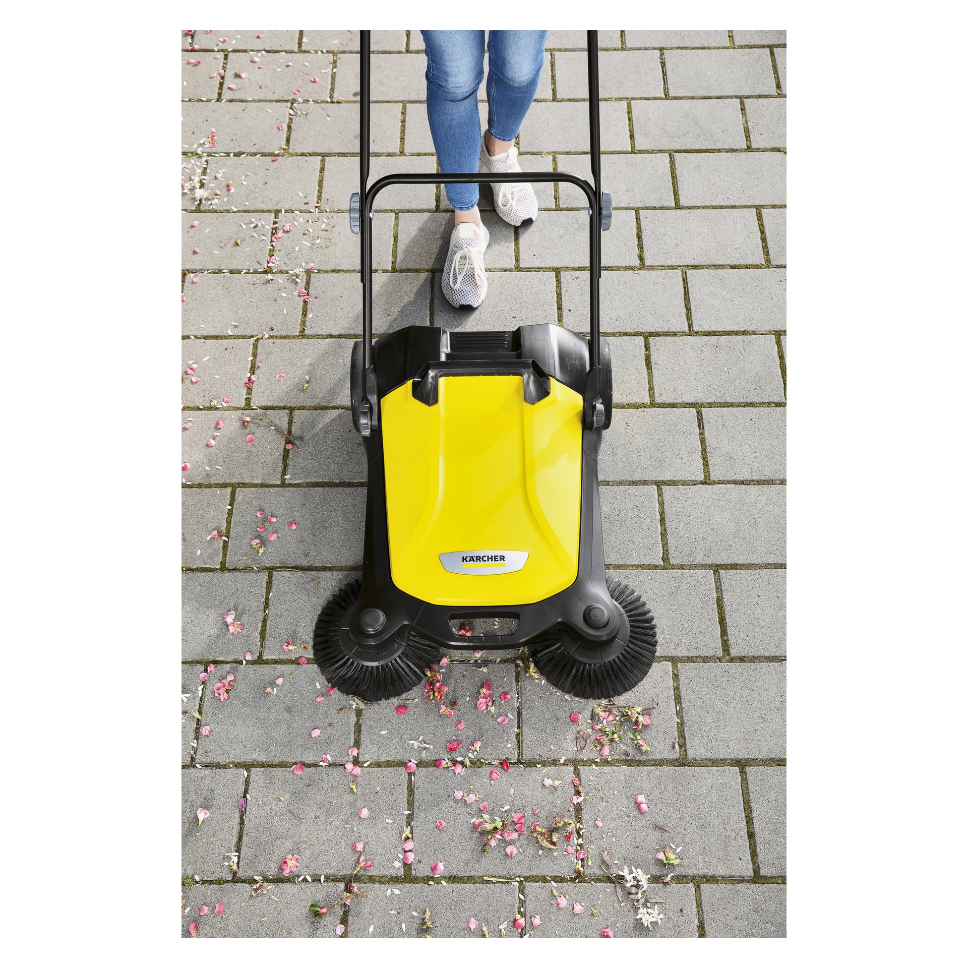 Noen opererer Kärcher Push Sweeper S4 Twin på grå asfalt, og feier opp rosa og hvitt rusk som ligger spredt på bakken.
