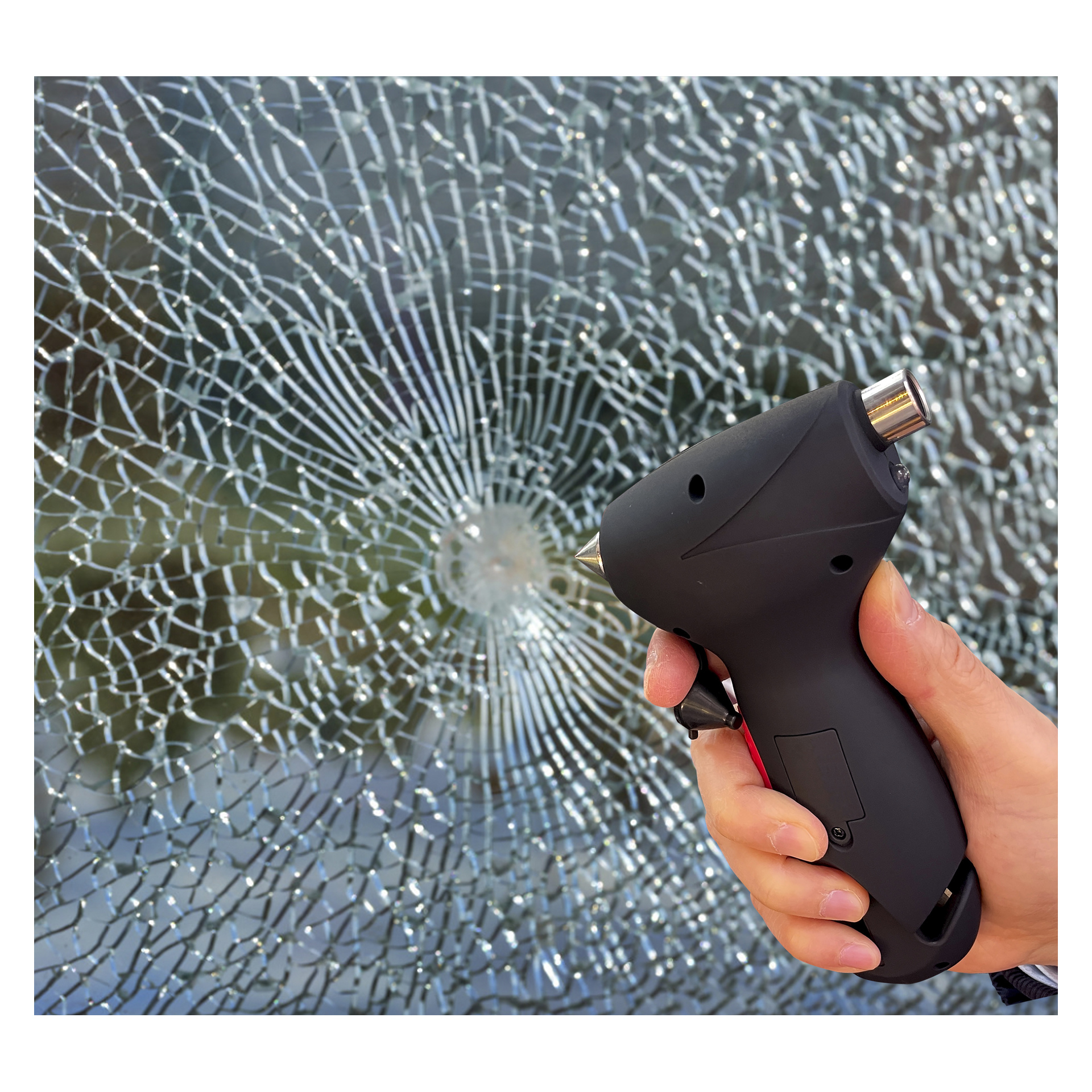 En hand håller Hamron 5-i-1-nödhammaren och siktar mot en cirkulär spricka i krossat glas med en suddig bakgrund synlig.