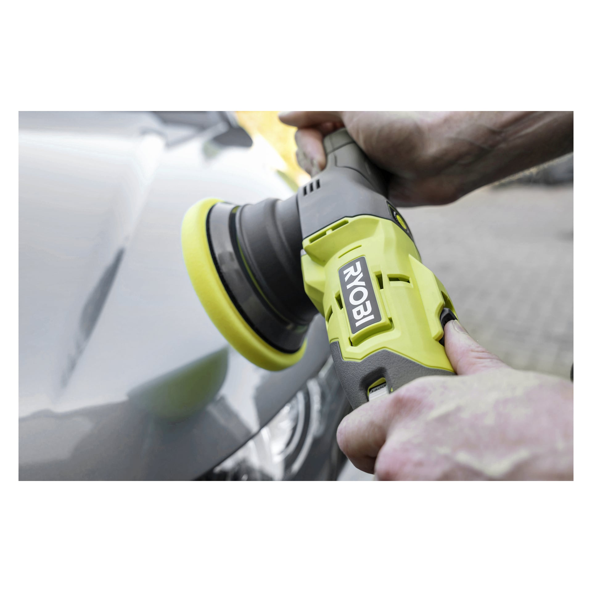 Händerna manövrerar en Ryobi One+ R18P-140 polermaskin med en gul pad på en grå bilhuv, Ryobi-märkning synlig på verktyget.