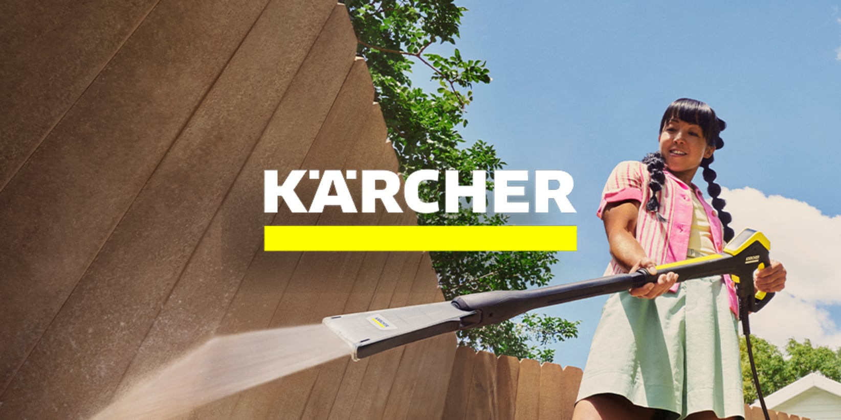 Kobieta czyści drewniane ogrodzenie na zewnątrz myjką ciśnieniową Kärcher; logo Kärcher i żółta linia widnieją na środku.