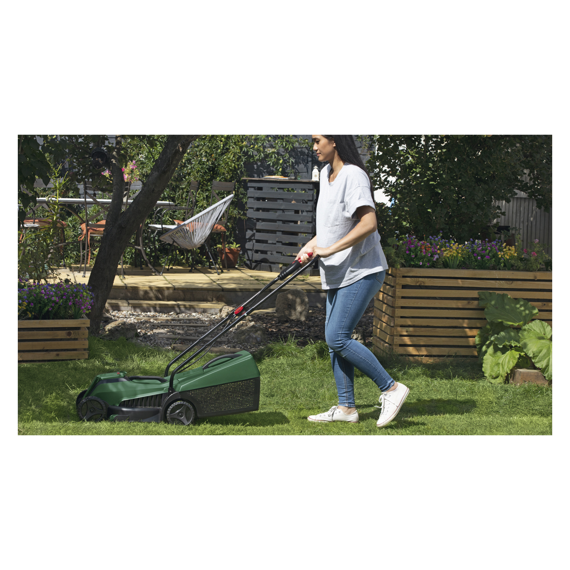 En person i vit t-shirt och jeans skjuter en Bosch Power 4 All klippare och trimmer genom en gräsbevuxen trädgård med planteringskrukor och hängmatta.
