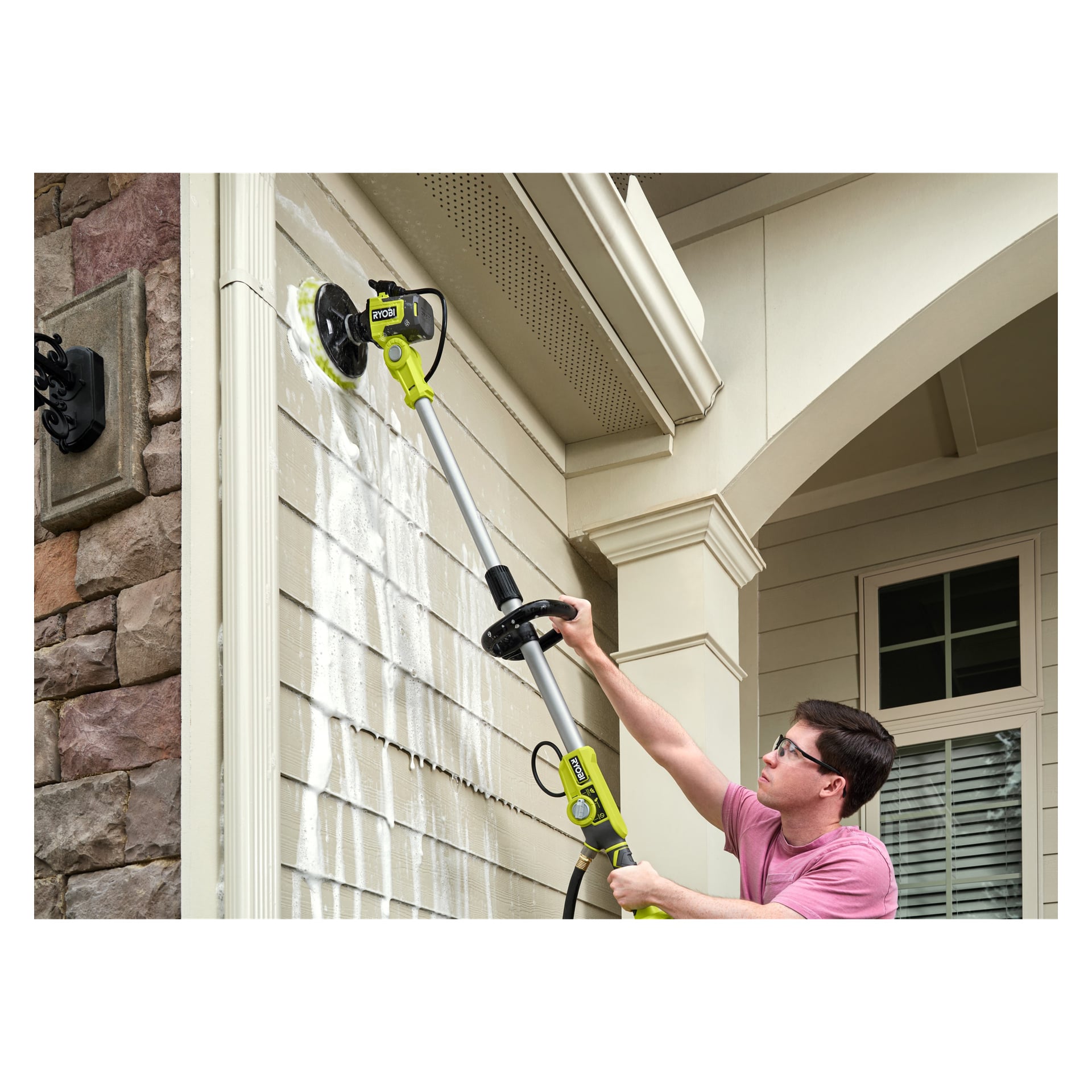 En person använder Ryobi One+ Cleaning brush RWTS18-1C20GJ med batteri och laddare för att tvätta sten och fasad vid taklinjen.