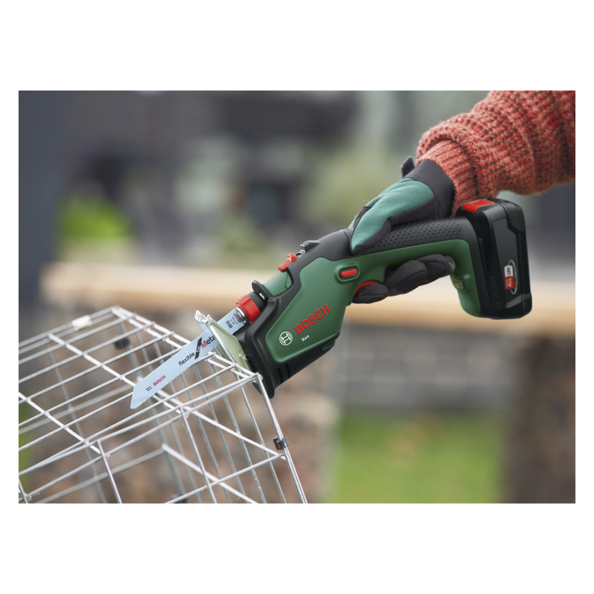 En person med handske använder en Bosch Power 4 All Keo batteribeskärningssåg för att såga metalltråd på en rektangulär bur utomhus.