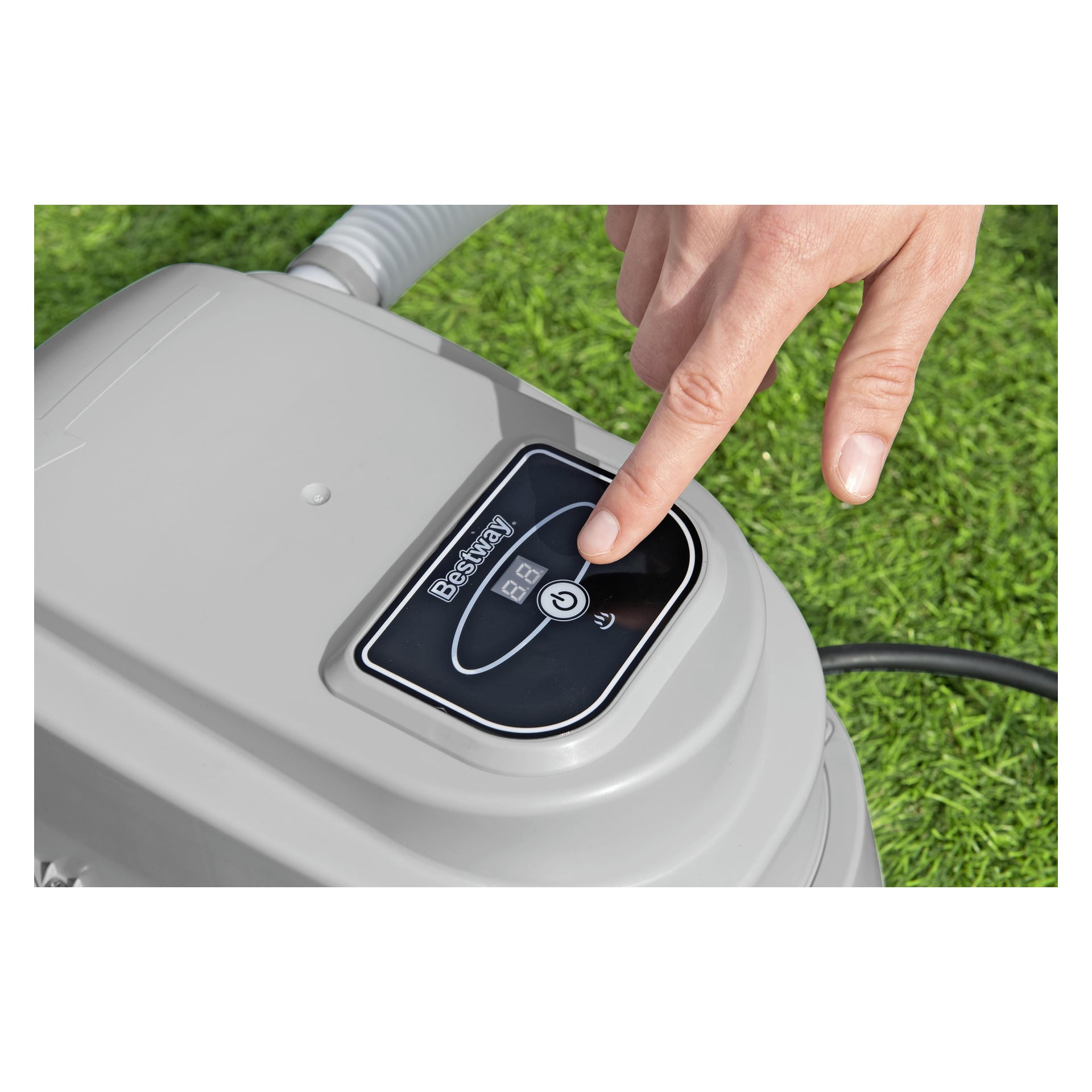En hand trycker på strömknappen på en Bestway Electric poolvärmare som visar 39, med den grå enheten stående på grönt gräs.