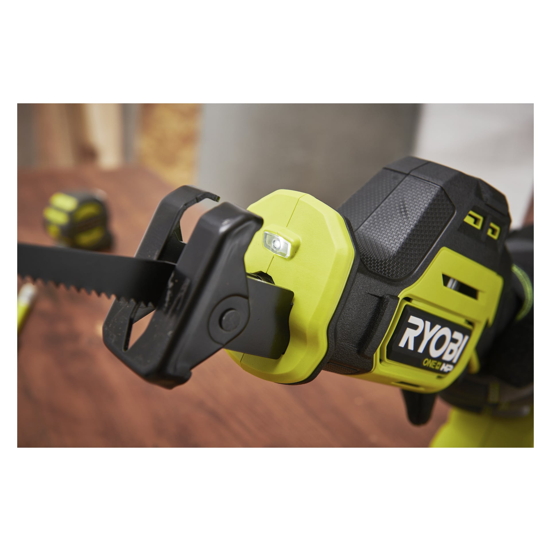 Ryobi One+ HP RRS18C1 batteridriven kolvsåg med svart blad på trä, suddigt måttband i bakgrunden.
