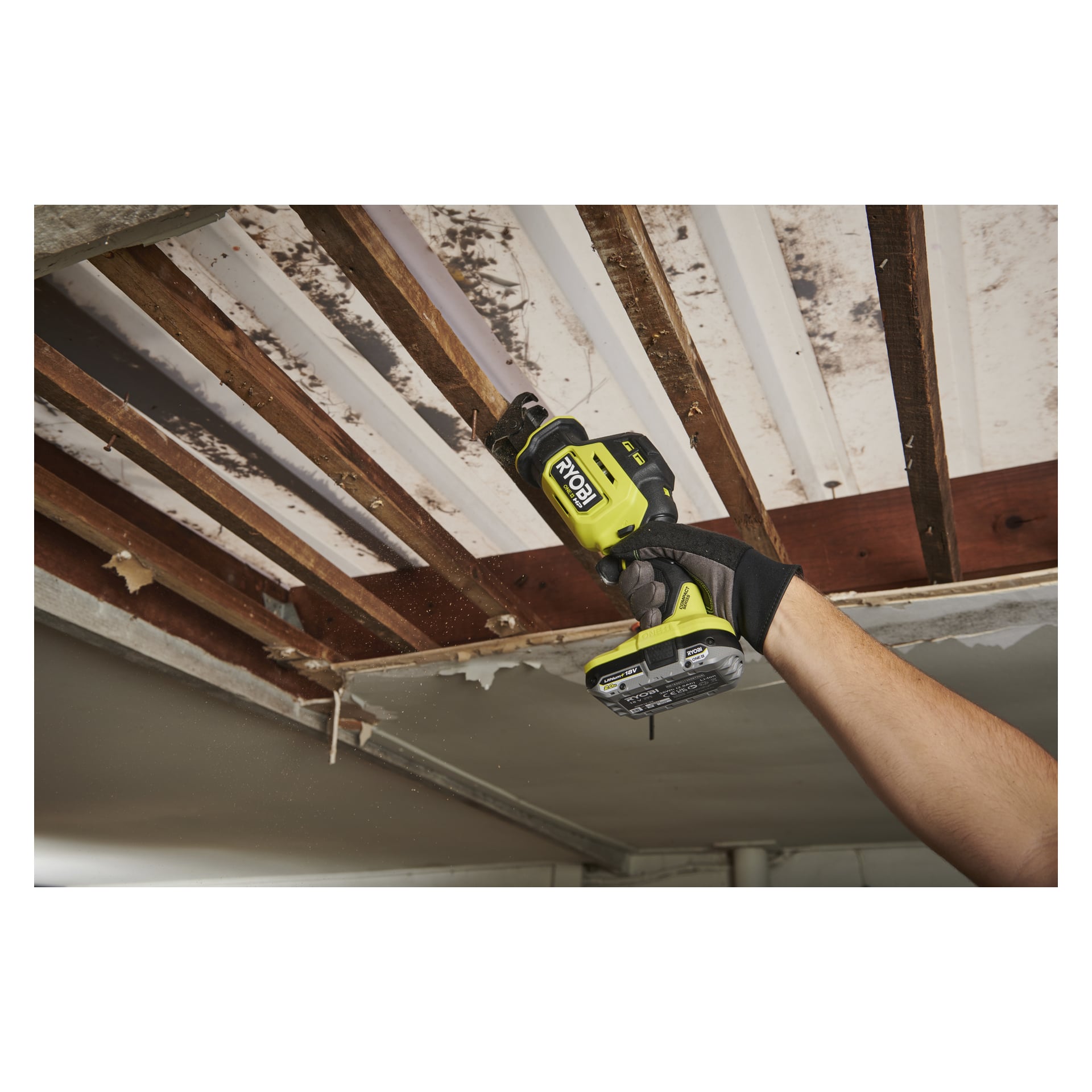 En person i svart handske använder en Ryobi One+ HP sladdlös bajonsåg för att såga en träbalk i ett korrugerat metalltak.