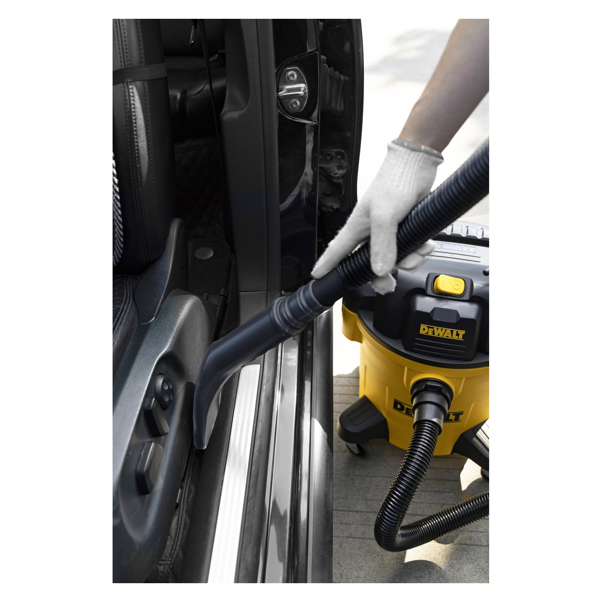 Med vit handske använder någon en DEWALT våt/torr dammsugare med ett smalt munstycke för att rengöra vid förarsätet i bilen.