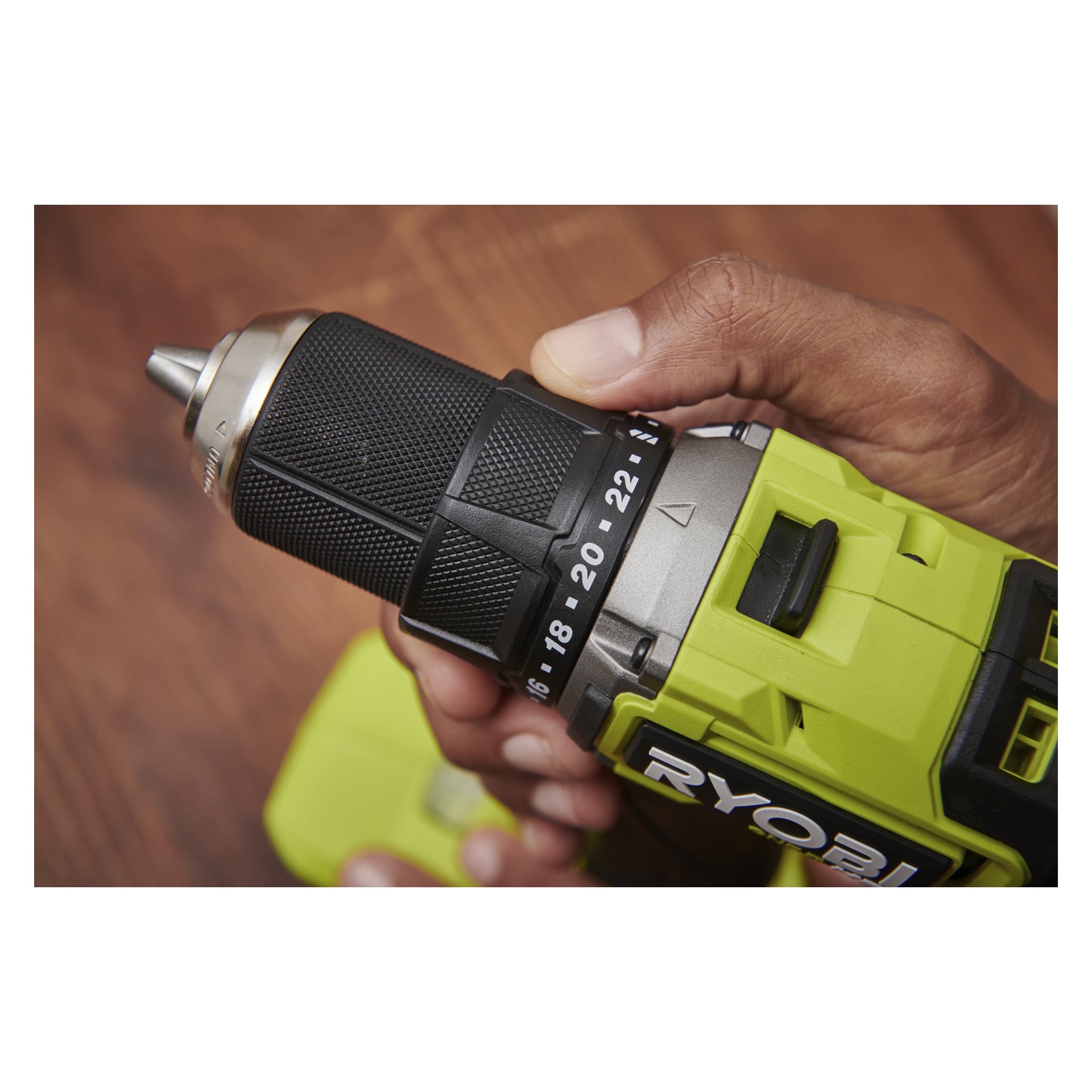 En person justerar vridmomentet på en Ryobi One+ HP Brushless borrmaskin RDD18C1-0, placerad ovanför en träyta.
