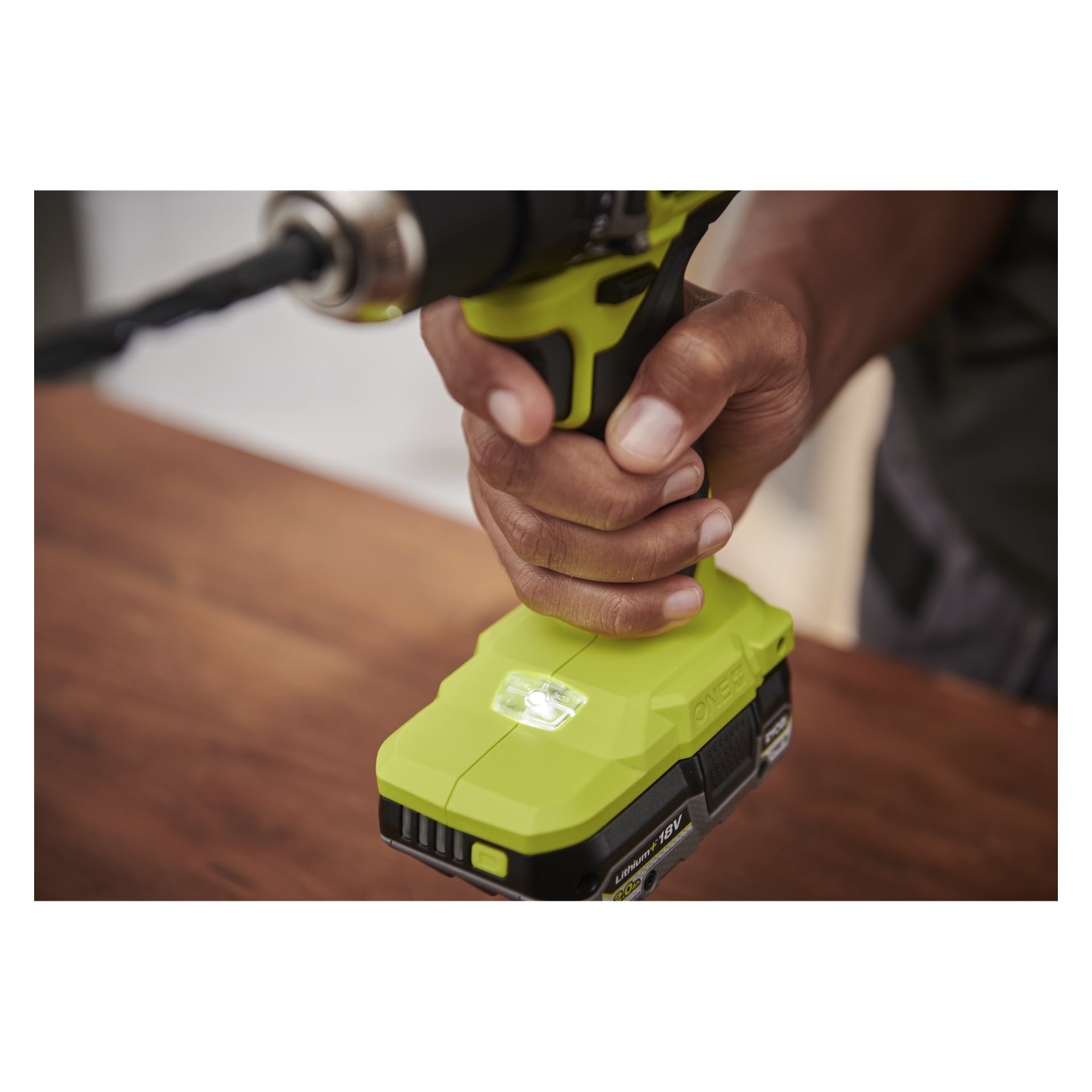 En hand greppar en Ryobi One+ HP Brushless RDD18C1-0 borr över trä, borrkrona pekande ut, baslampan lyser.